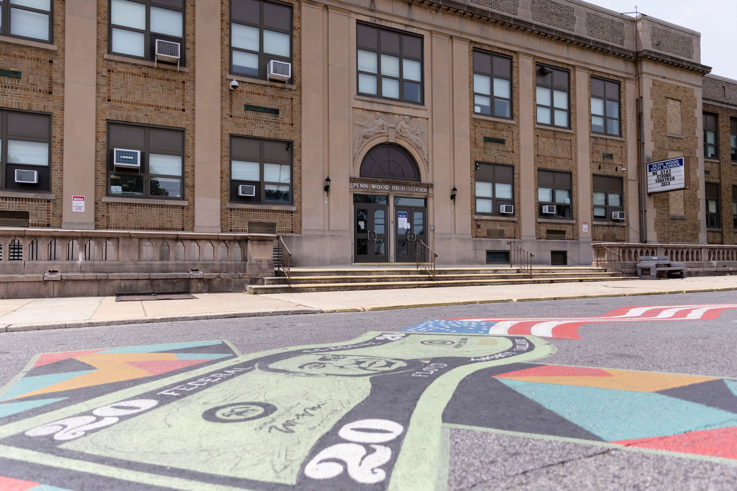A colorful mural on the ground in front of a large brick building.