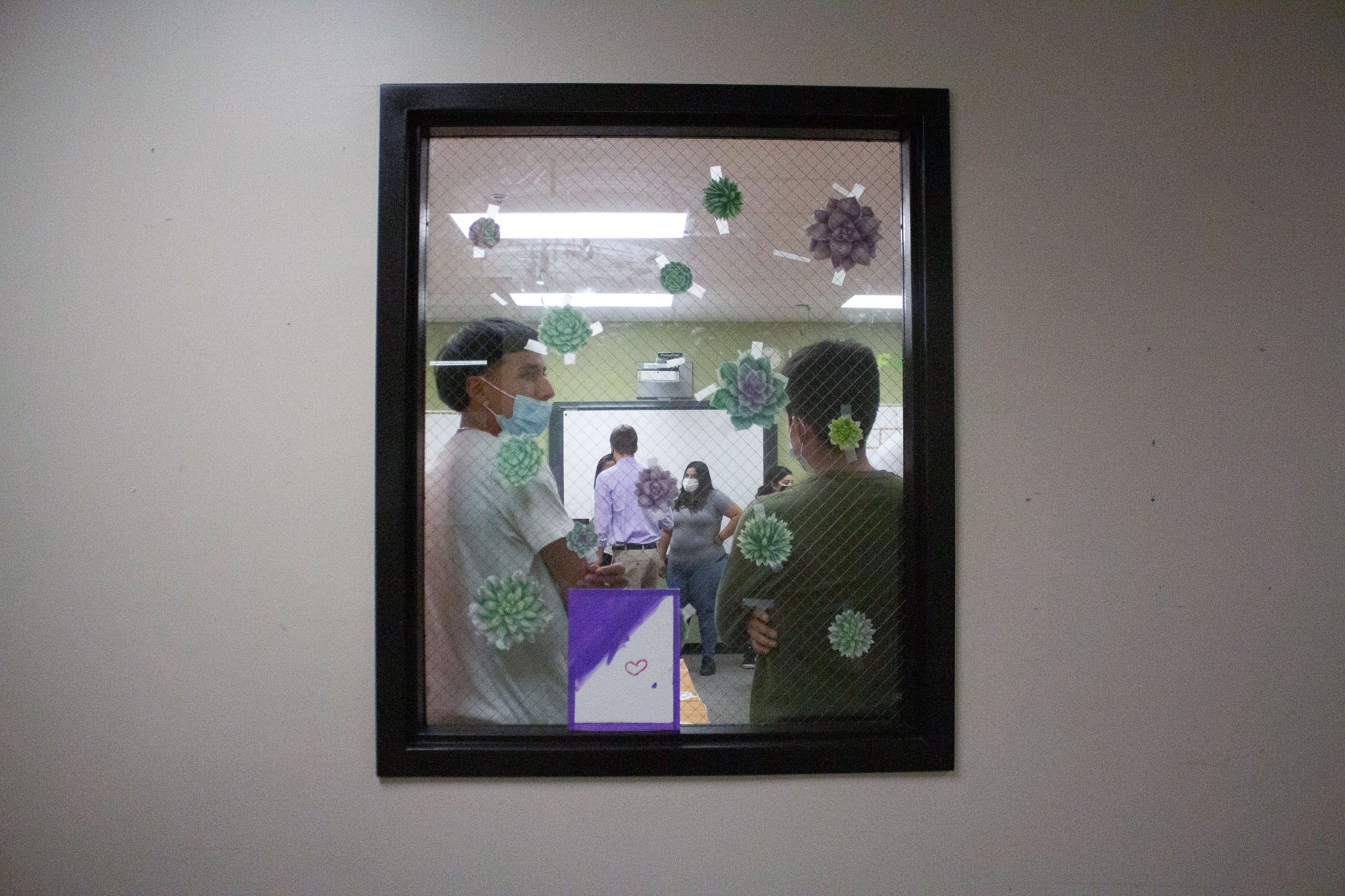 Two students are framed by a window decorated with decals. One student wears a blue face mask.