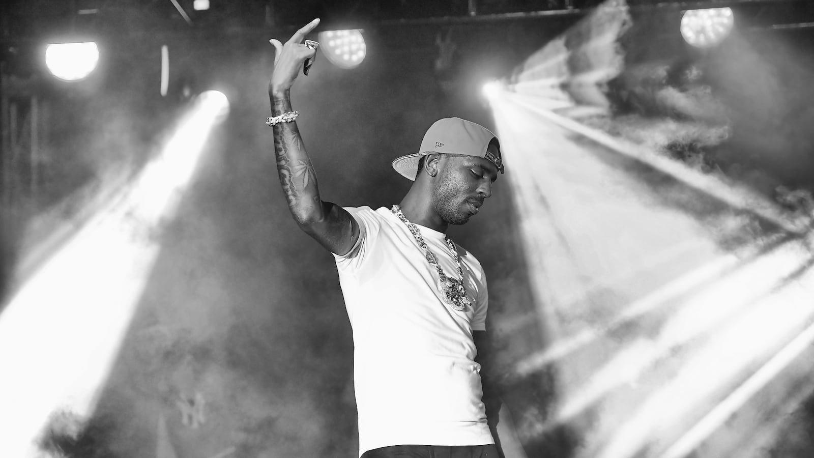 A black and white photograph of Memphis rapper Young Dolph gesturing on stage during a performance, pointing in the air as lights cascade across the background.