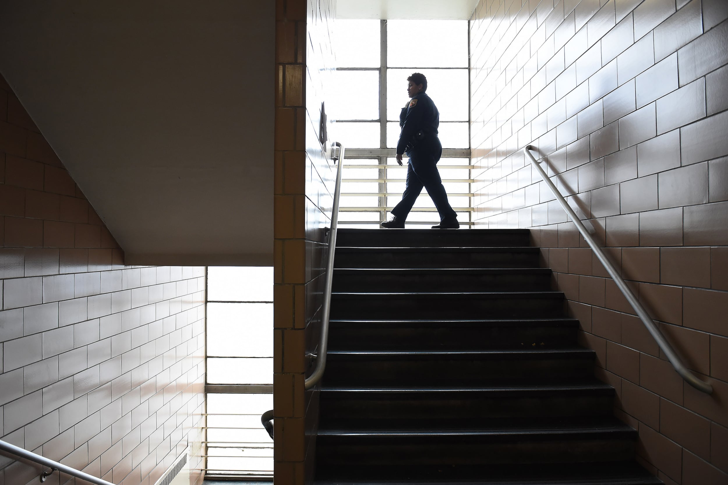 A photograph of a silhouette of a woman in a uniform walking across a stairwell of a school building.
