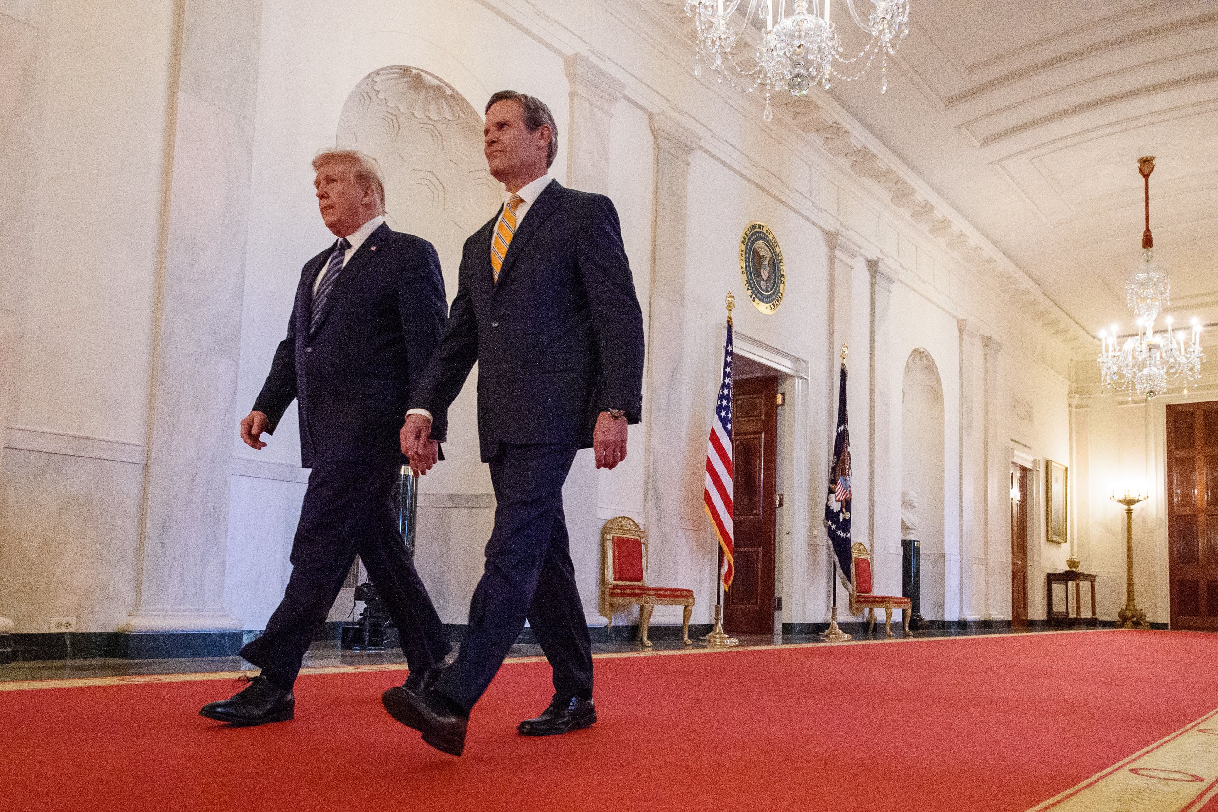 Tennessee Governor Bill Lee walks behind former President Donald Trump on a red carpet within the White House.