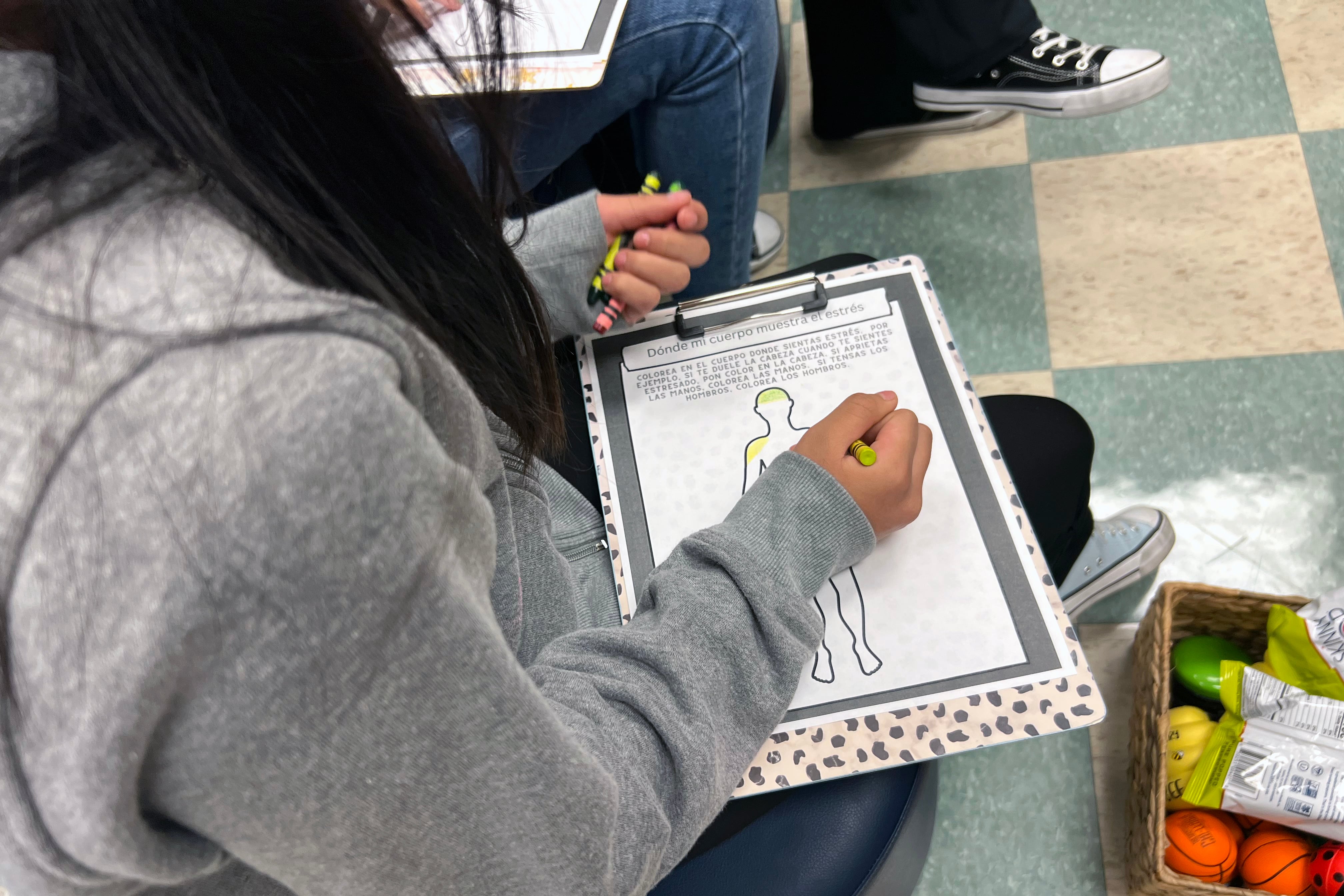 A student at Brighton Park Elementary School uses a crayon to color inside an outline of the human body.