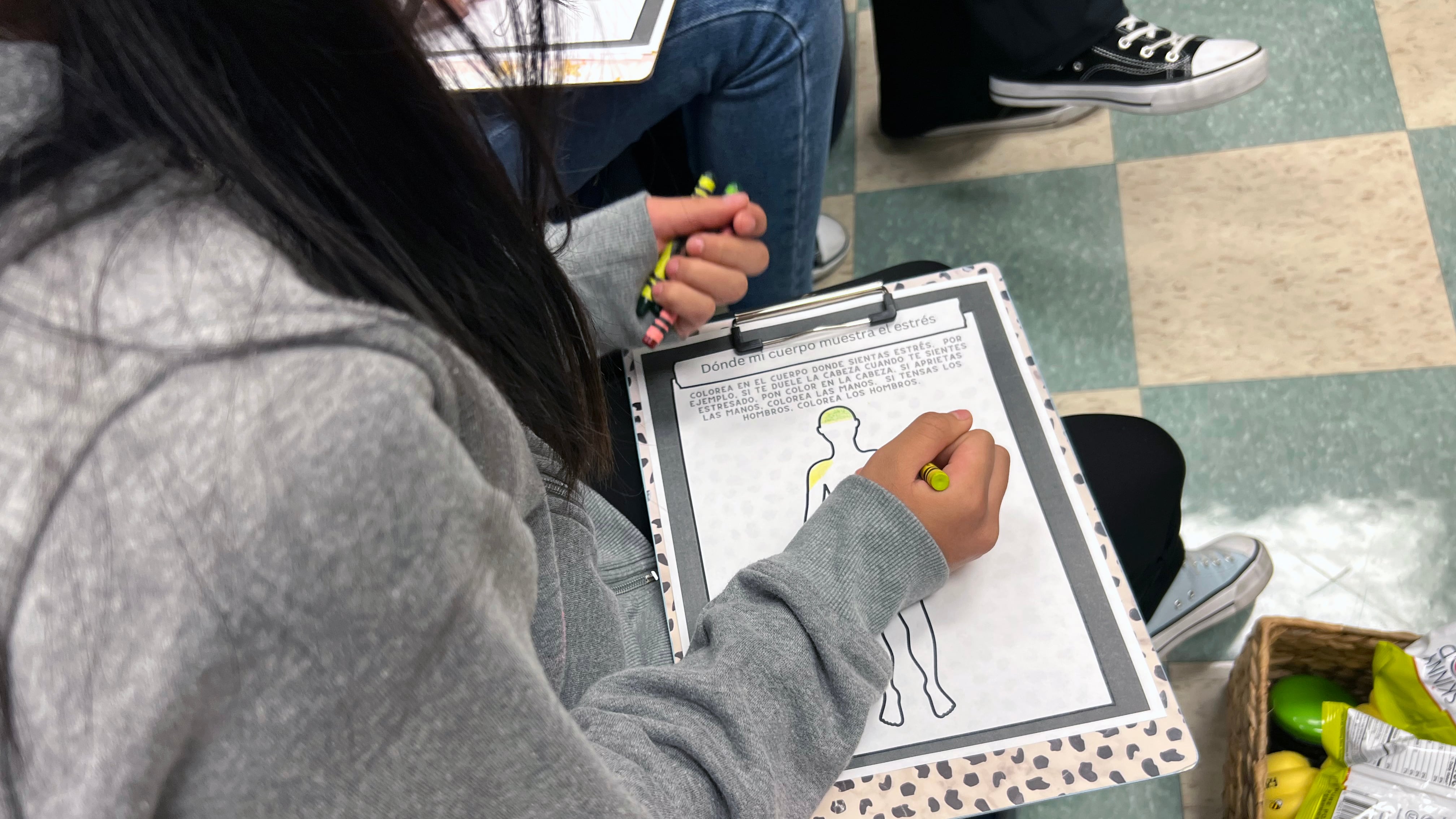 A student at Brighton Park Elementary School uses a crayon to color inside an outline of the human body.