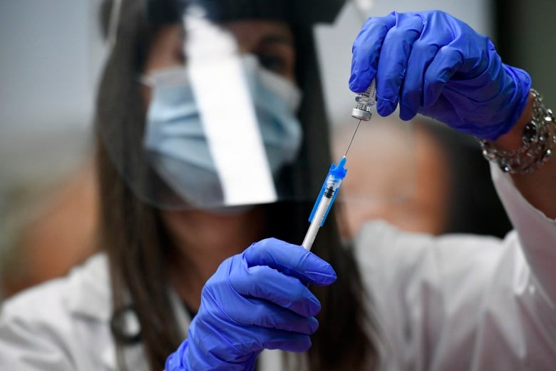 A health care worker wearing a mask and a face shield uses a syringe to measure out a dose of the COVID-19 vaccine from a vial.