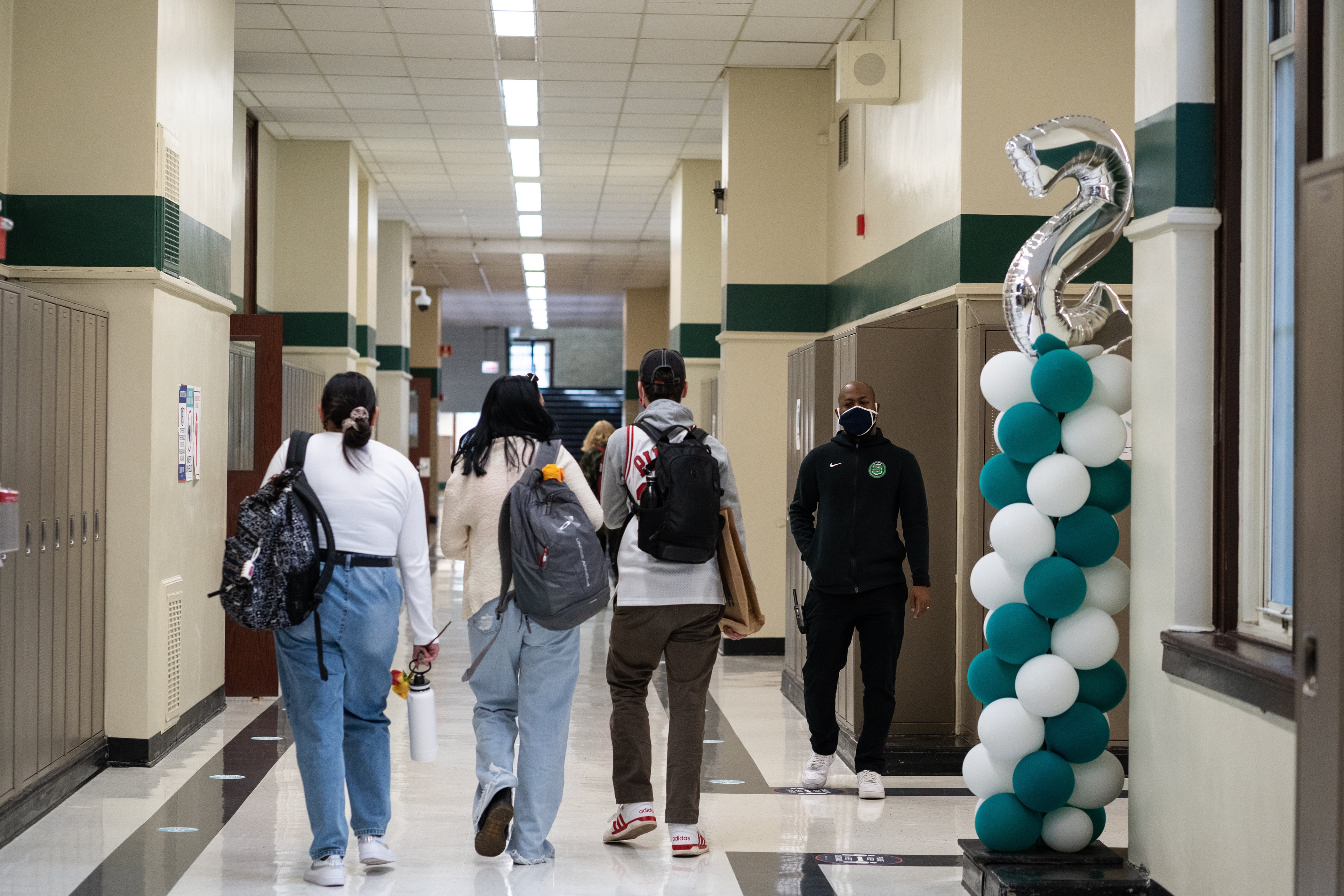 Students with backpacks in a school hallway. The hall is decorated with balloons.