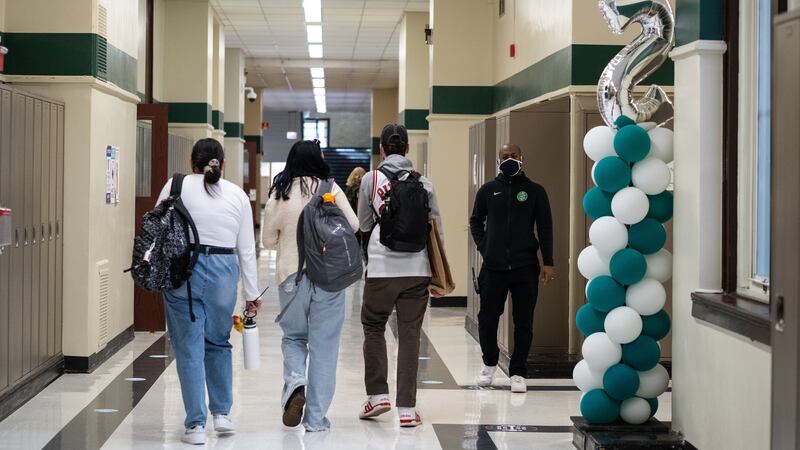 Students with backpacks in a school hallway. The hall is decorated with balloons.