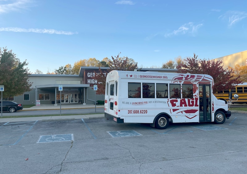 A white bus with red writing on the side is parked in front of a school.