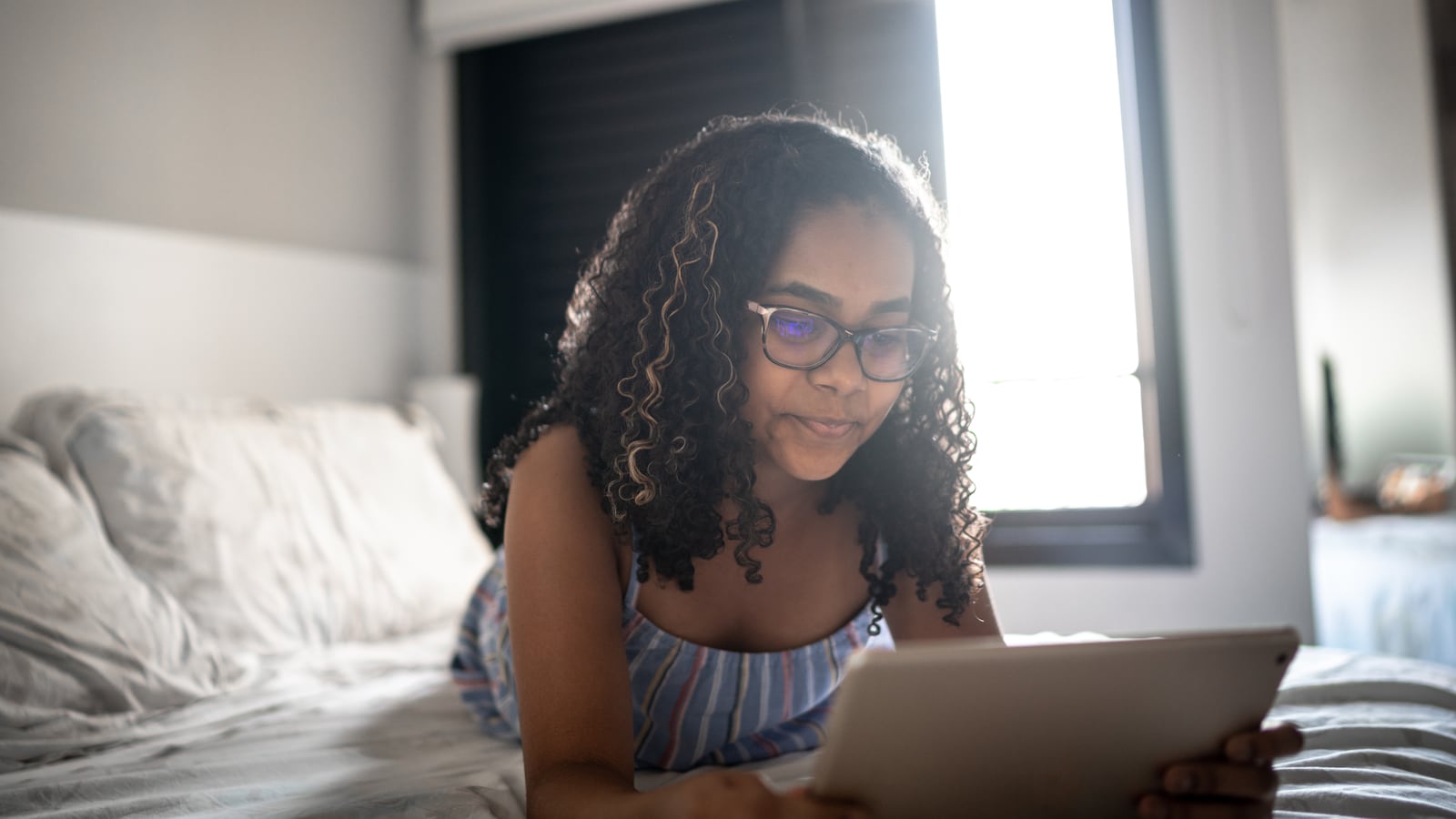 Teenager wearing a tank top and glasses reads on digital tablet at home