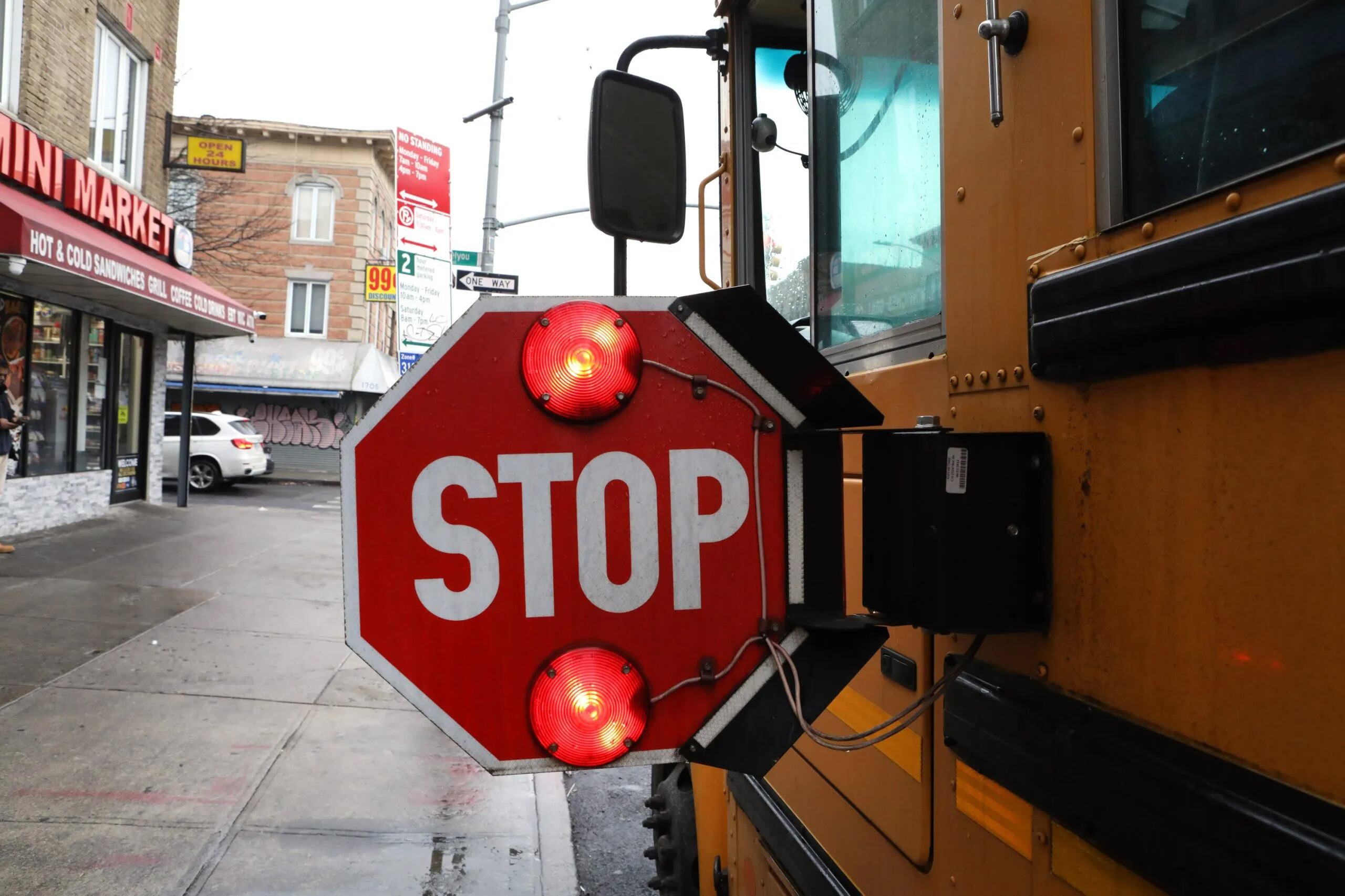 A large red and white stop sign on the side of a yellow school bus with a street corner in the background.
