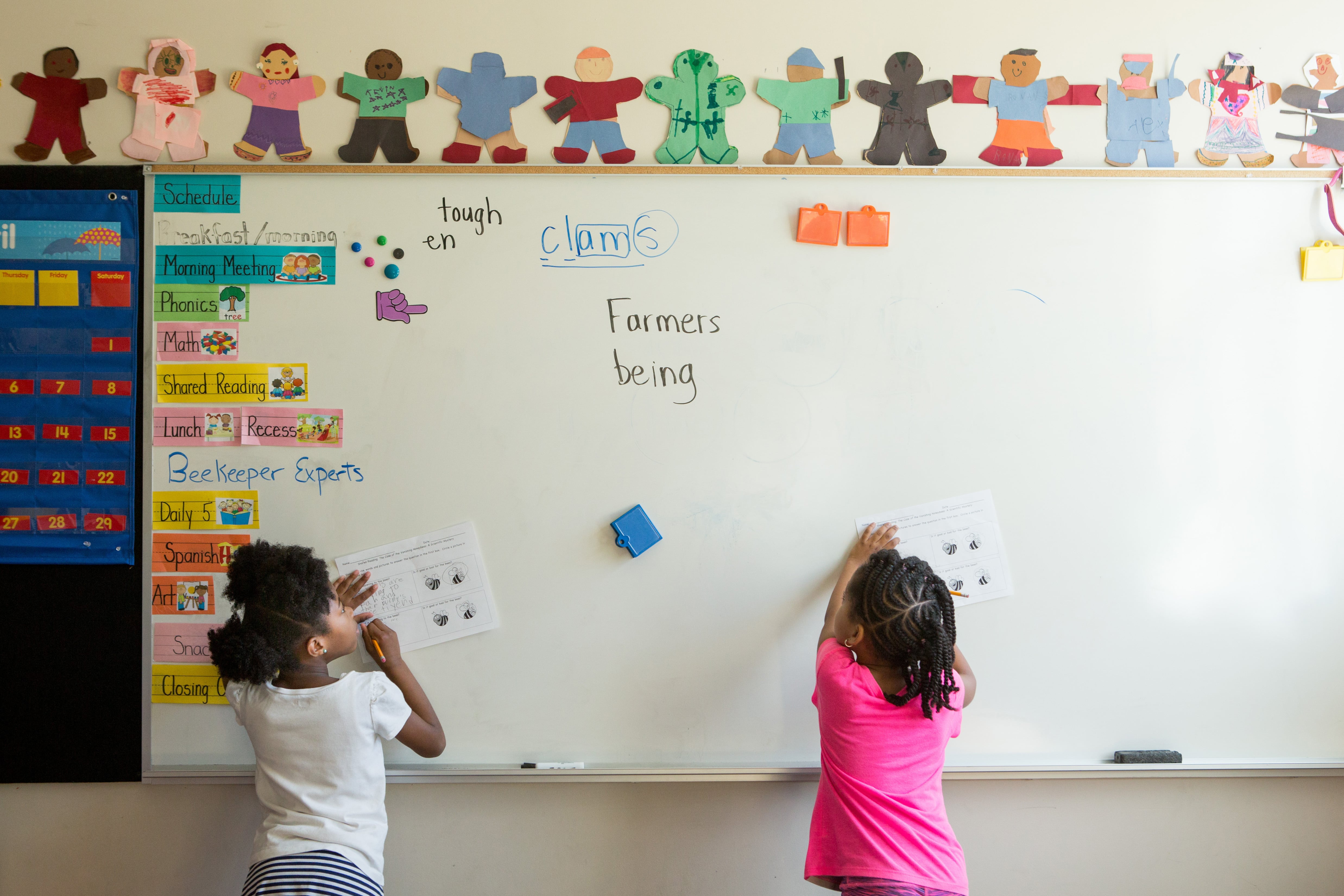 Two first grade girls stand at a white board and answer questions for a project about bees.