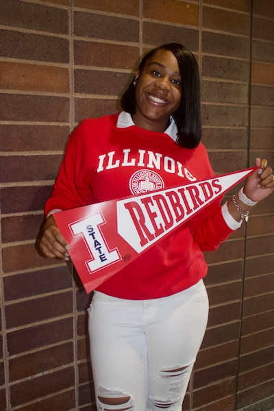 A high school senior with dark hair and wearing a red sweater and holding a university pendant poses for a portrait.