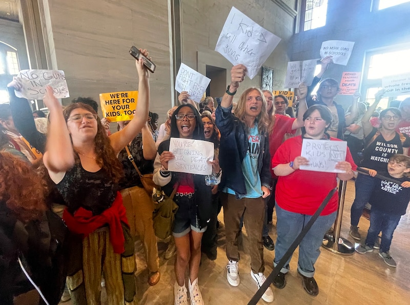 A group of students and other people shout and hold signs during a protest inside a large building.
