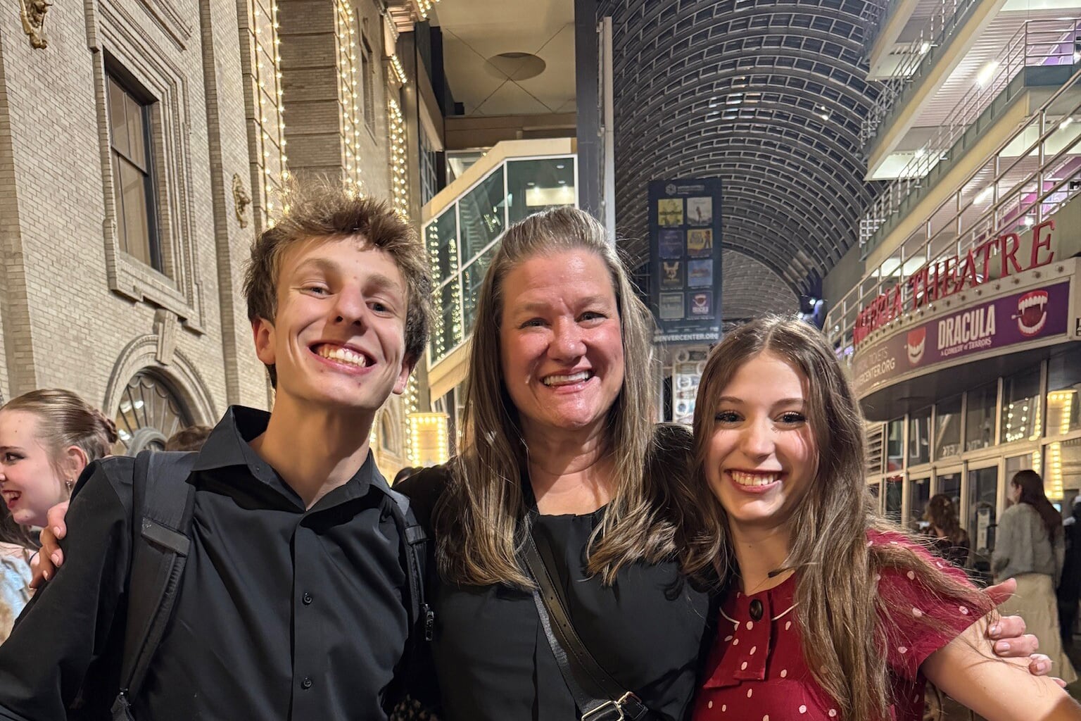 An adult poses with two high school students while all three stand side by side embracing while smiling for a portrait.