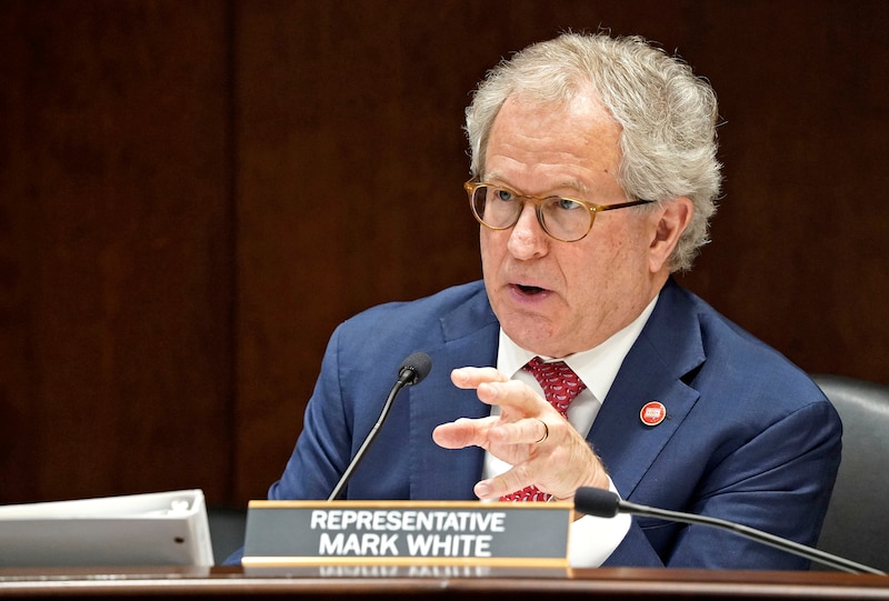 Man in a suit and tie gestures while speaking into a mic.