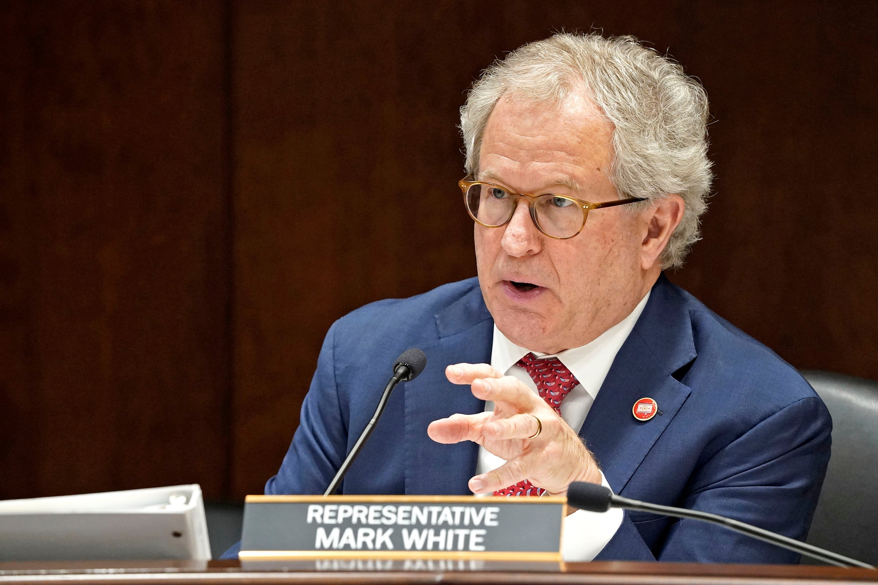 Man in a suit and tie gestures while speaking into a mic.