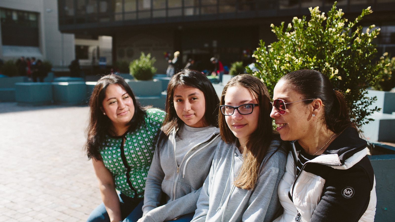 From left, Lordes Lliguichiuzhca, her daughter Elizabeth Cuzco, 13, Sonia Bucur, 13, and her mother Dina Bucur, sit in front of Martin Luther King High School after attending the Round 2 high school fair.