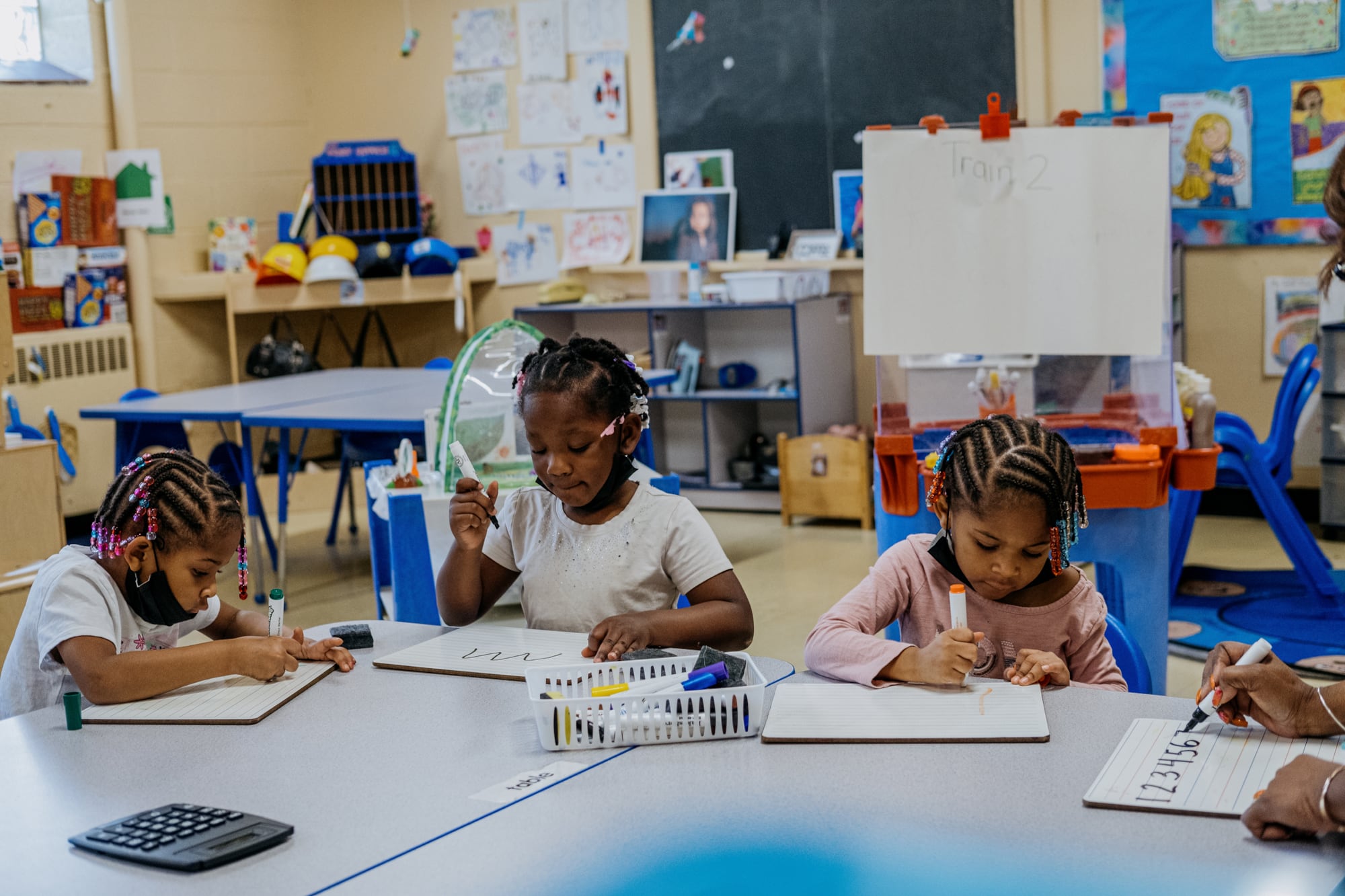 Young children sit side by side at their desks in a classroom.