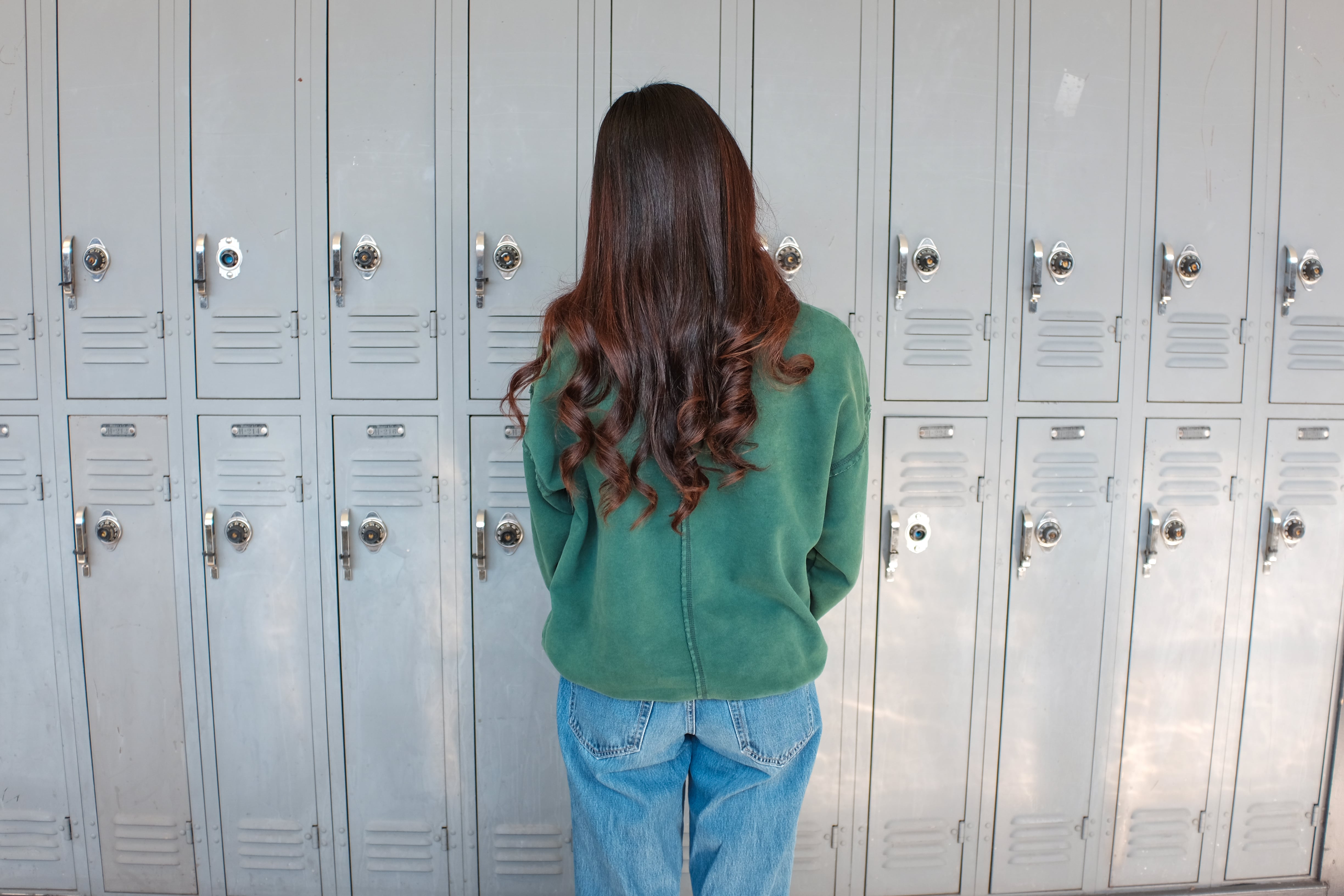 A female student in a green top faces a wall of lockers.