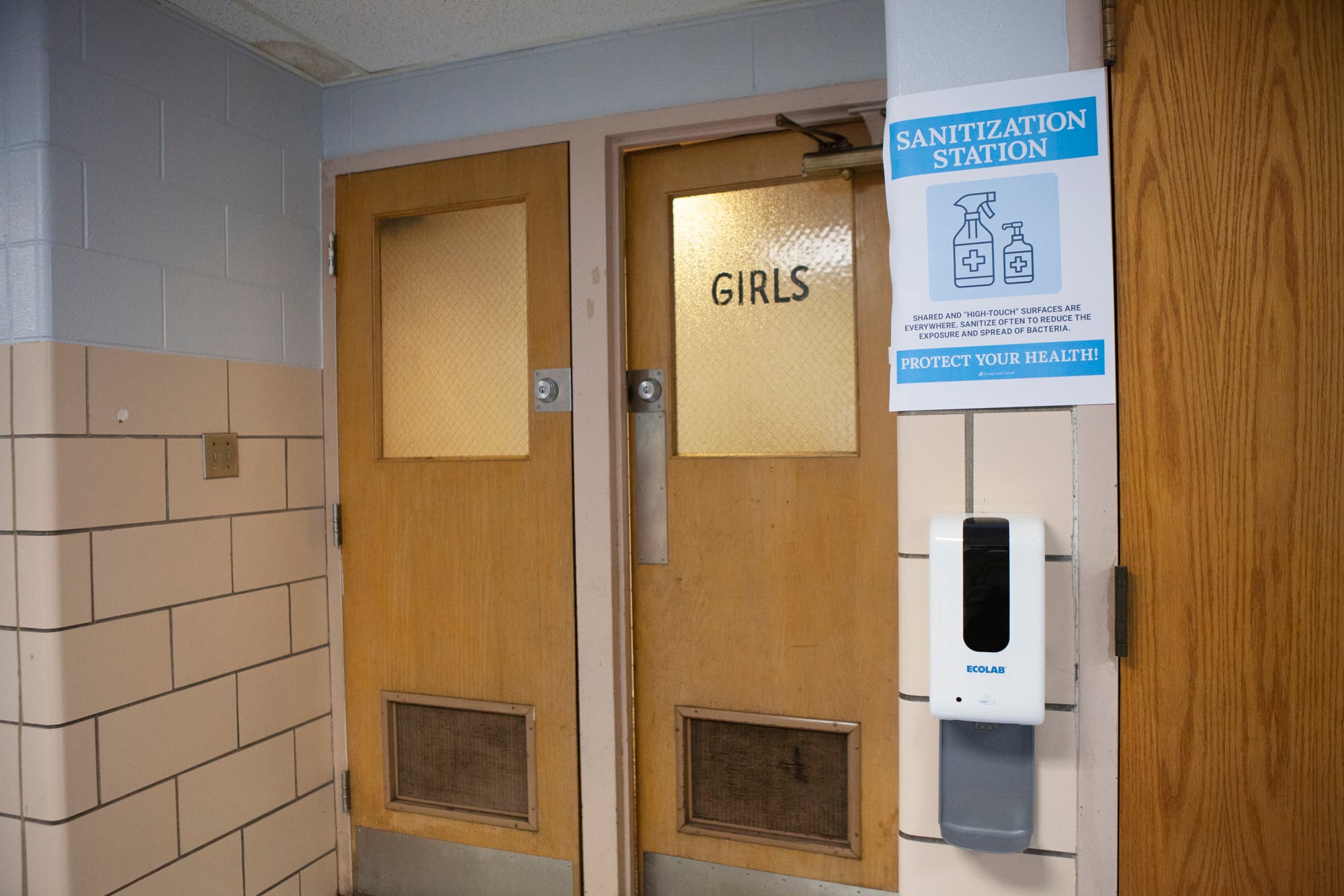 A sign outside a girls bathroom indicating a sanitization station.