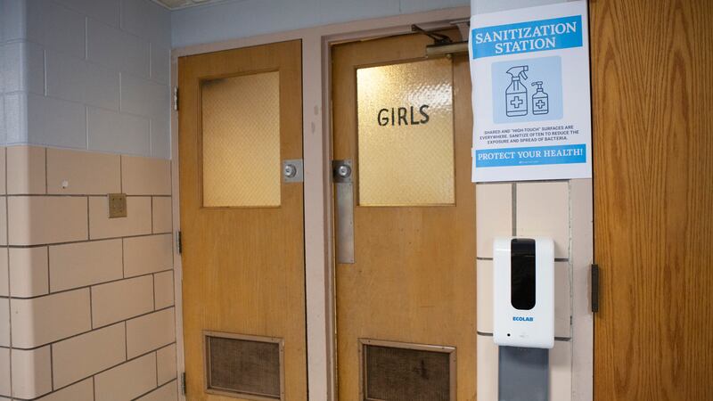 A sign outside a girls bathroom indicating a sanitization station.
