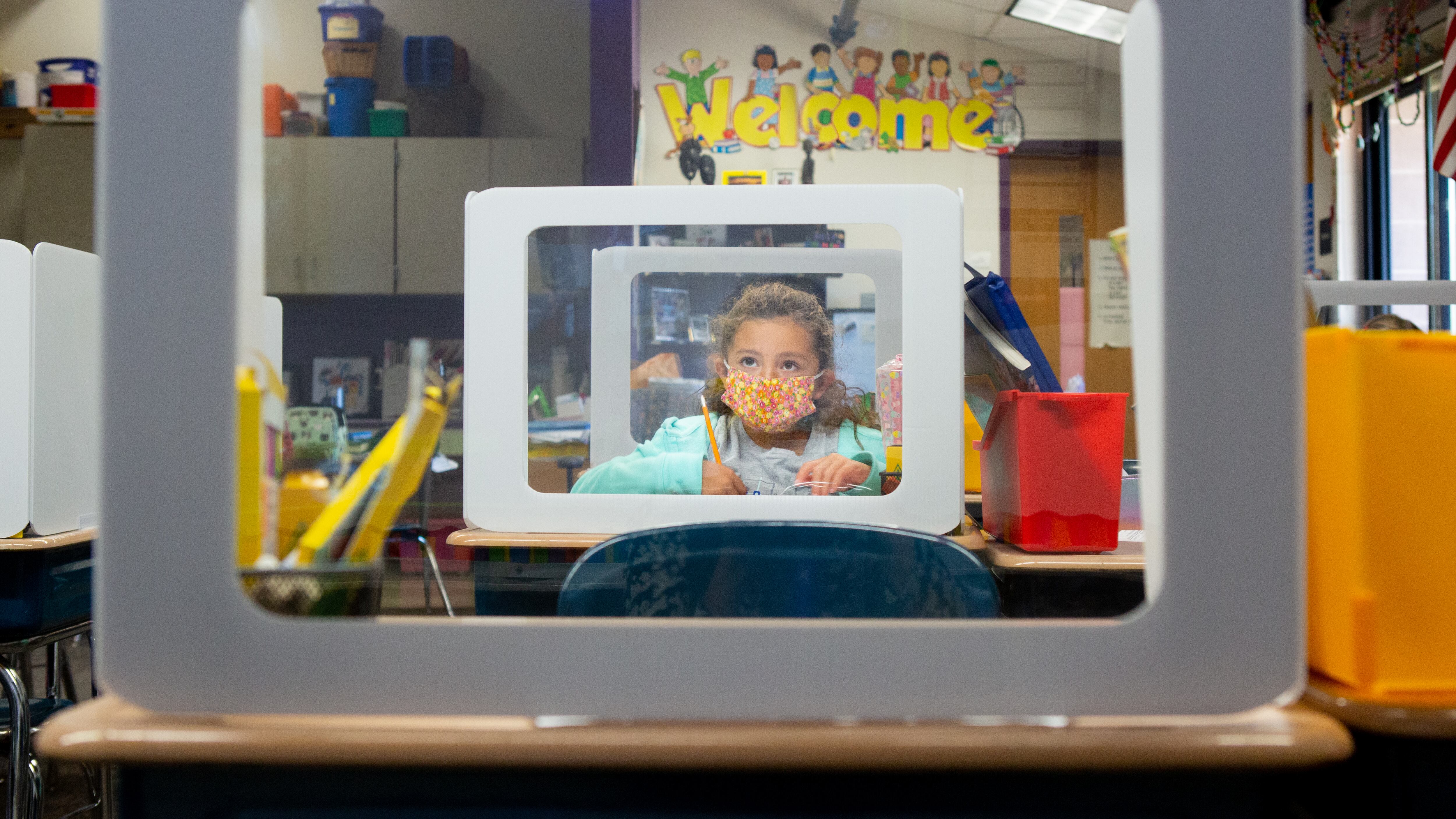 A young elementary student depicted on a computer screen behind a desk screen