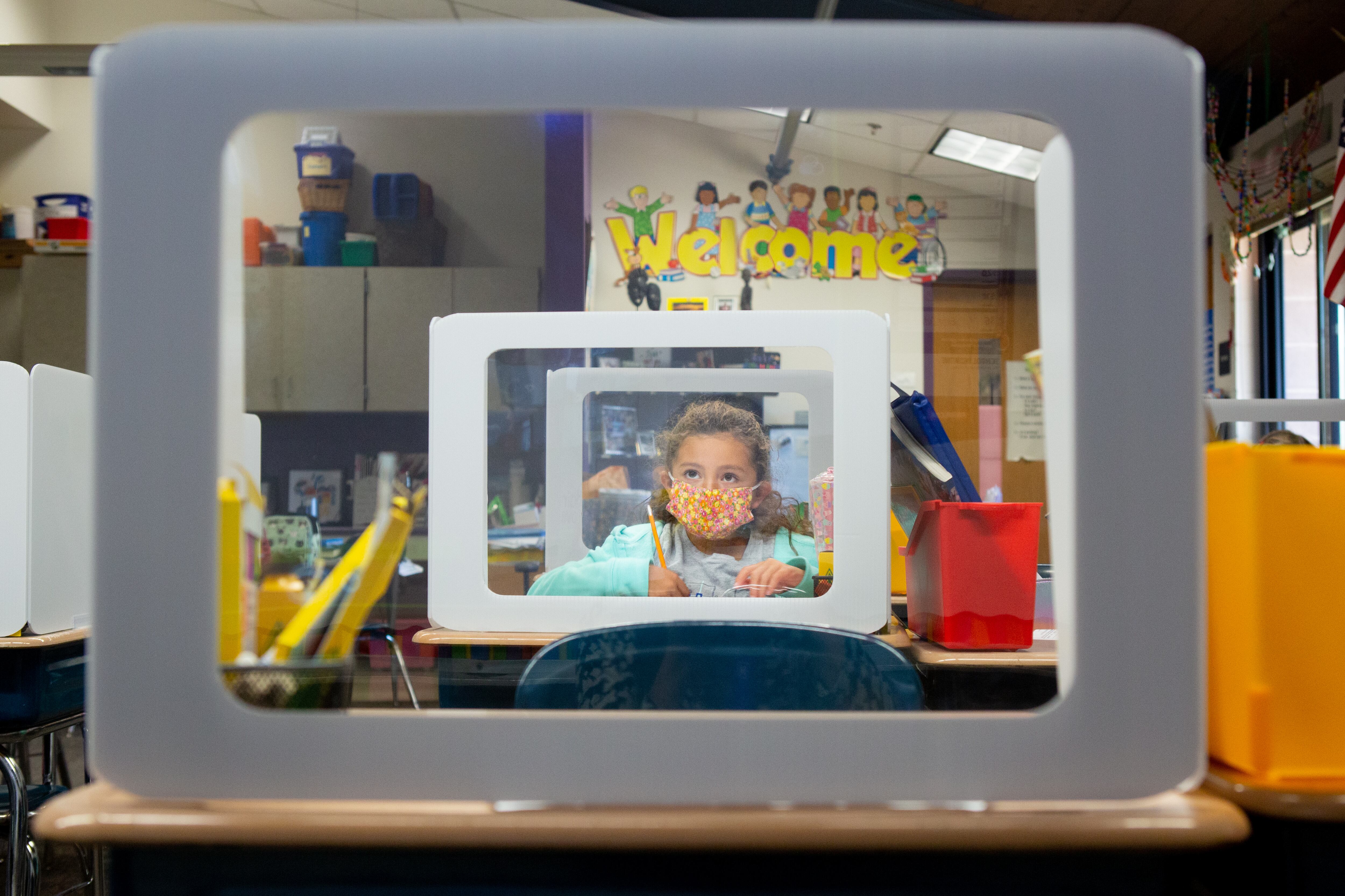 A young elementary student depicted on a computer screen behind a desk screen