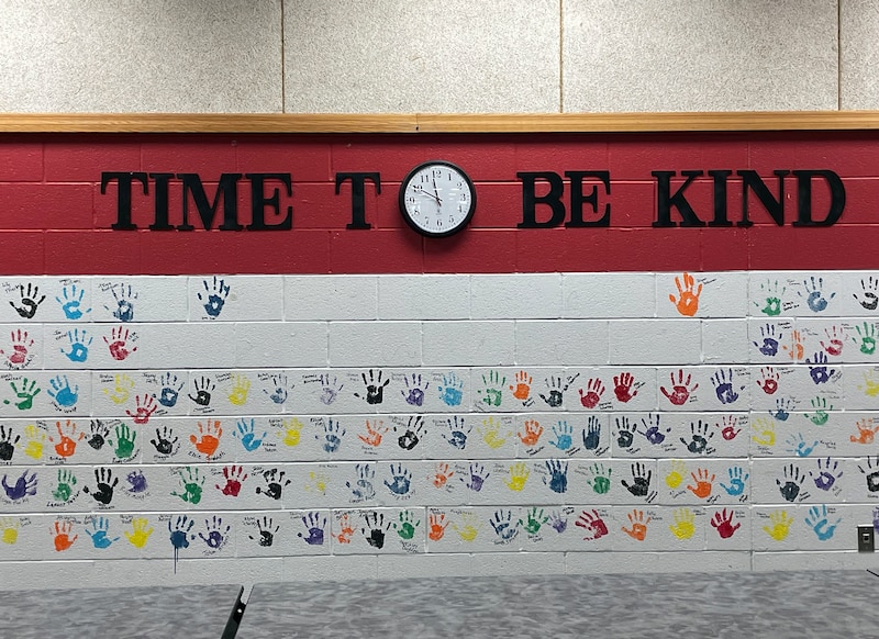 A mural on a concrete brick wall that reads "Time to be kind" and lots of colorful handprints.