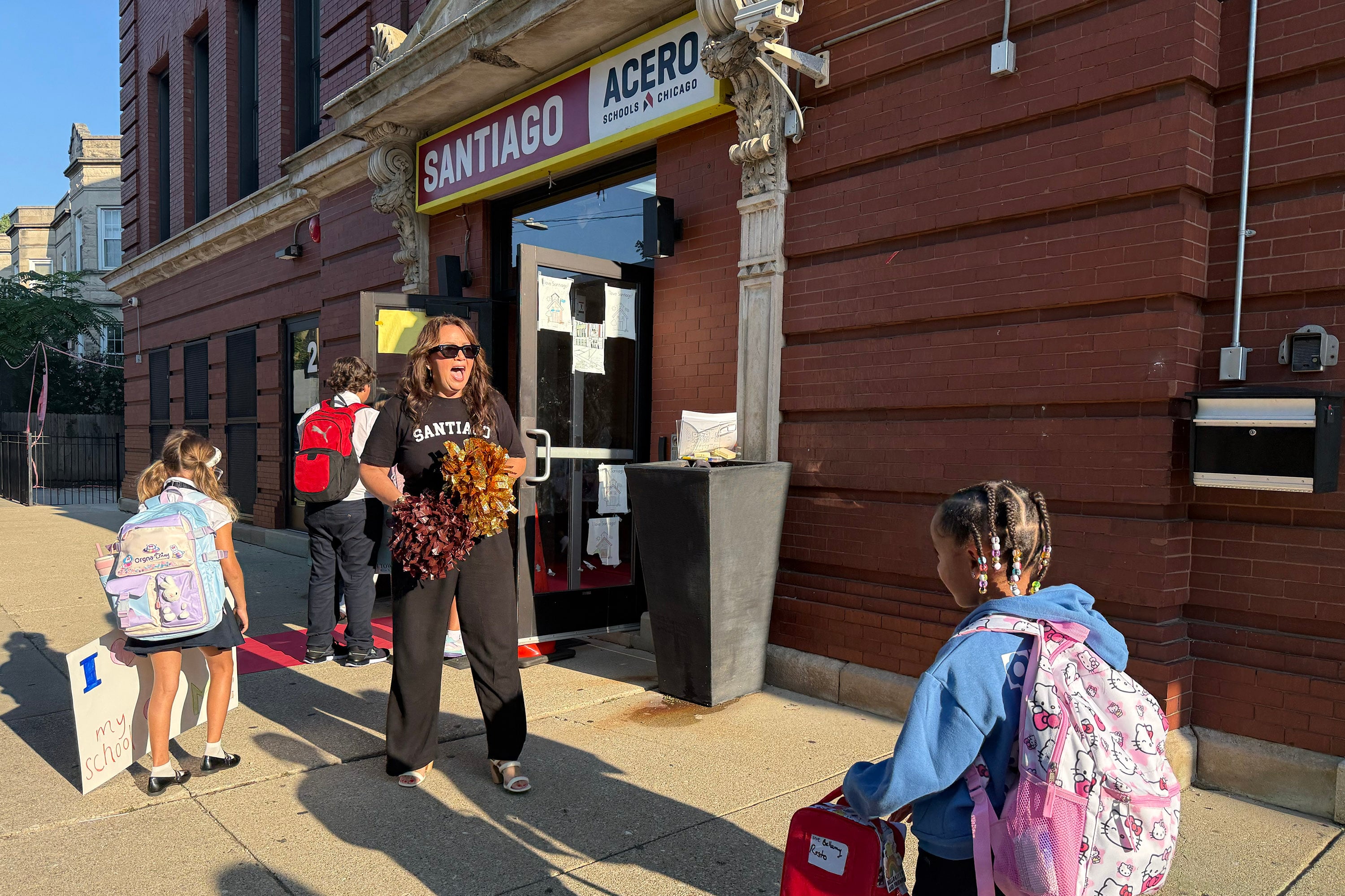 A photograph of adults and students greeting each other outside of a brick school building.