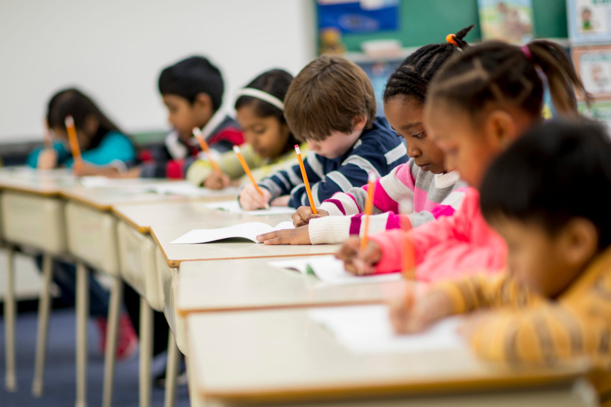 A row of students working on school work at desks in a classroom.