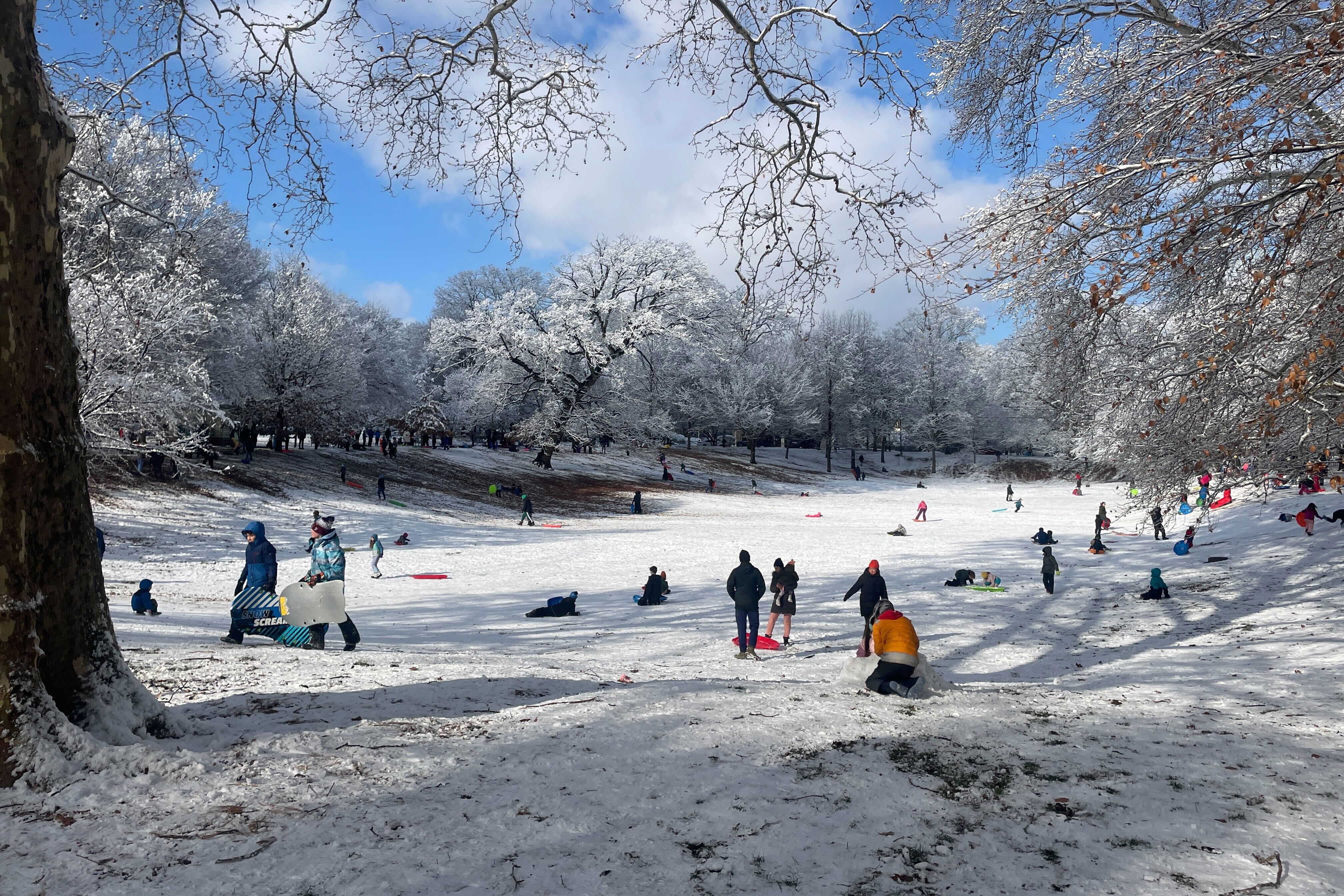 A photograph of a giant snow covered park with children in coats and carrying sleds.