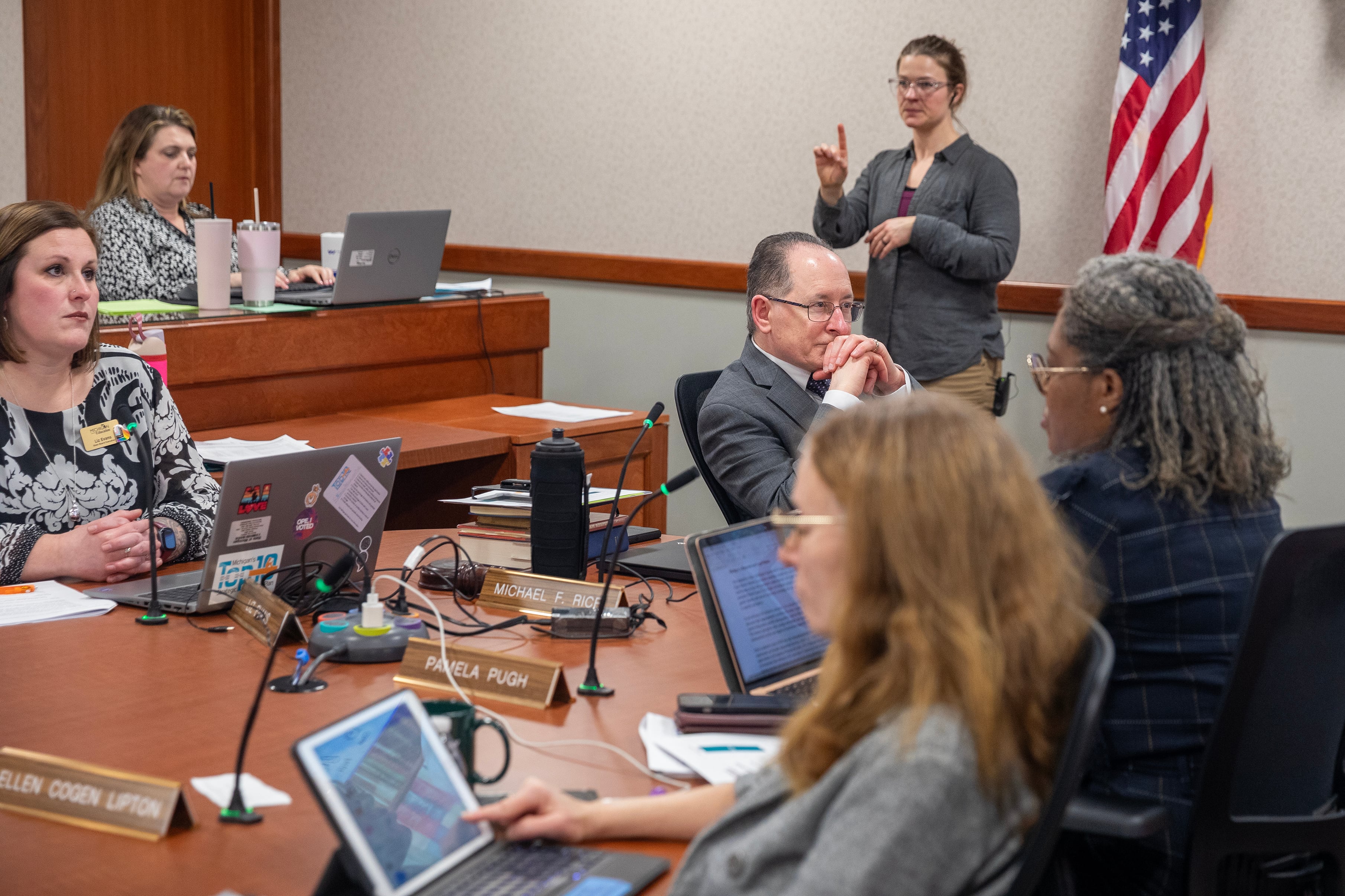 A group of people in business clothes sit at a wooden table in a conference room.