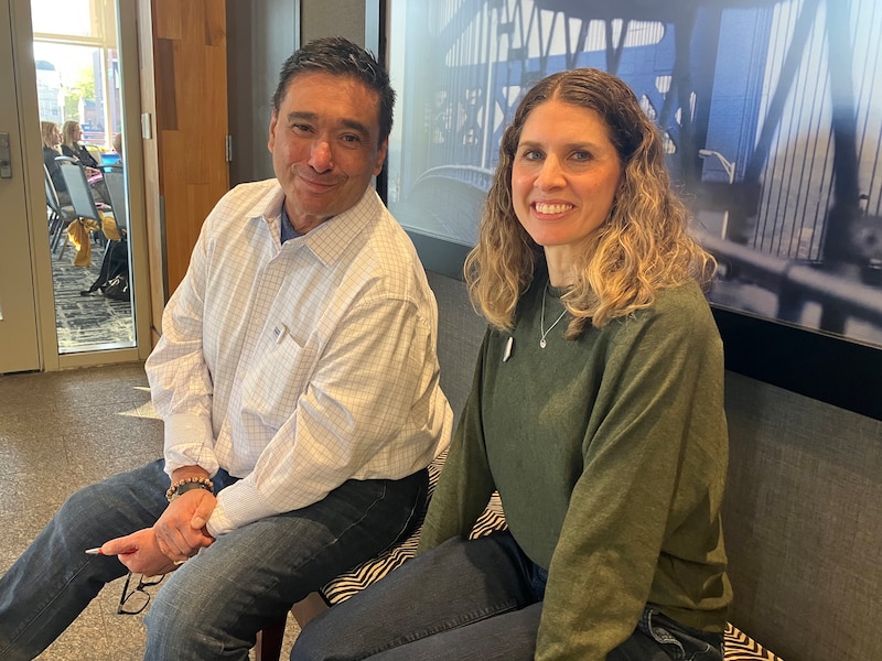 A photograph of a man and woman sitting next to each other on a bench posing for a portrait.