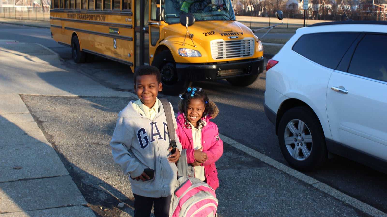 Two young children stand in front of a yellow school bus.