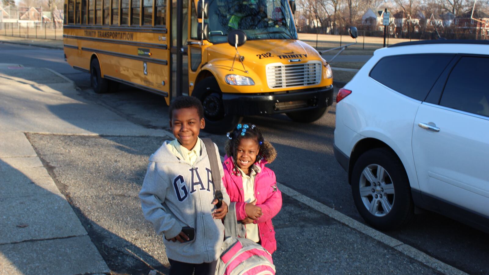 Two young children stand in front of a yellow school bus.