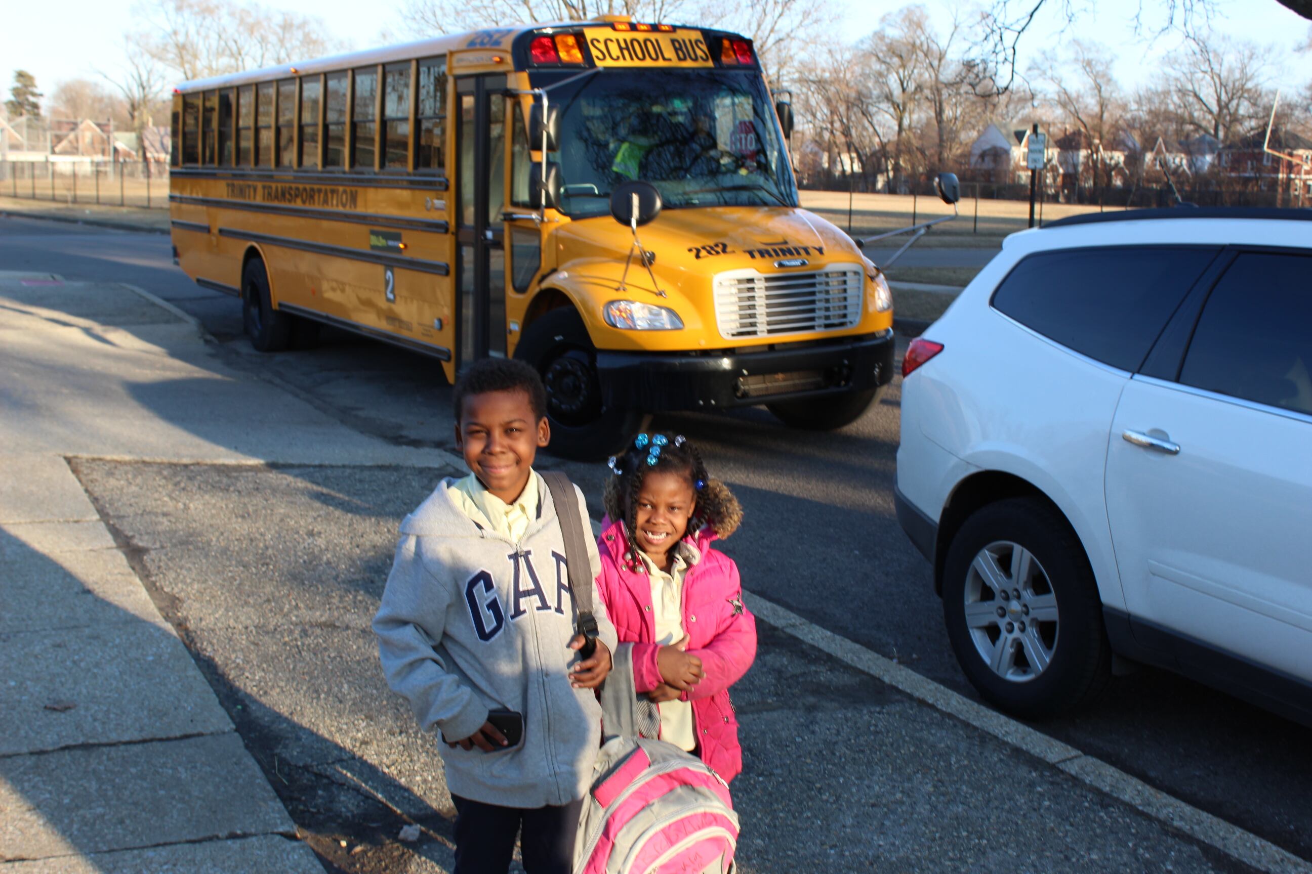 Two young children stand in front of a yellow school bus.