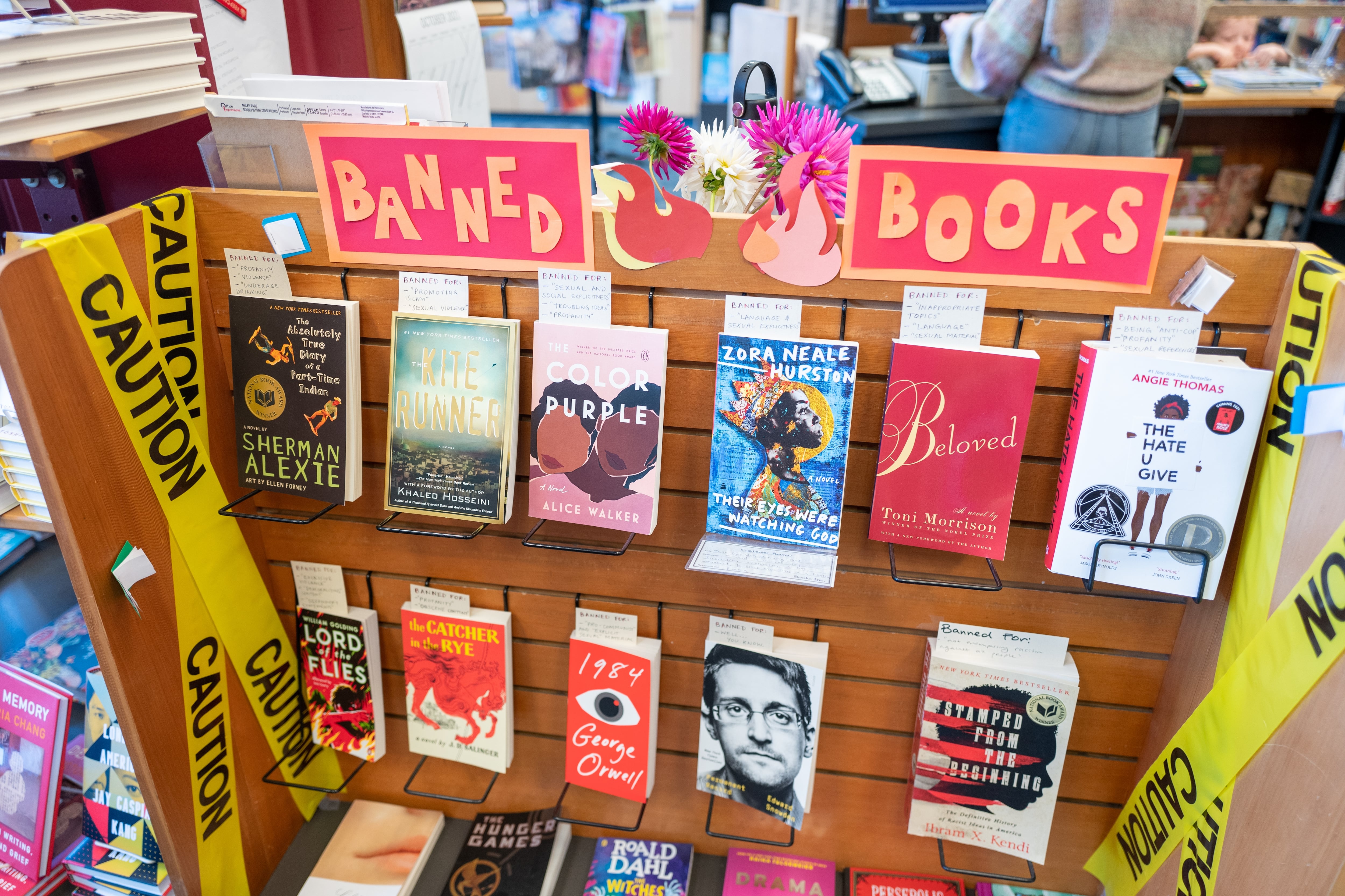 A section of books in a bookstore are marked with a sign and yellow caution tape as “Banned Books”.