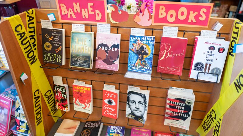 A section of books in a bookstore are marked with a sign and yellow caution tape as “Banned Books”.