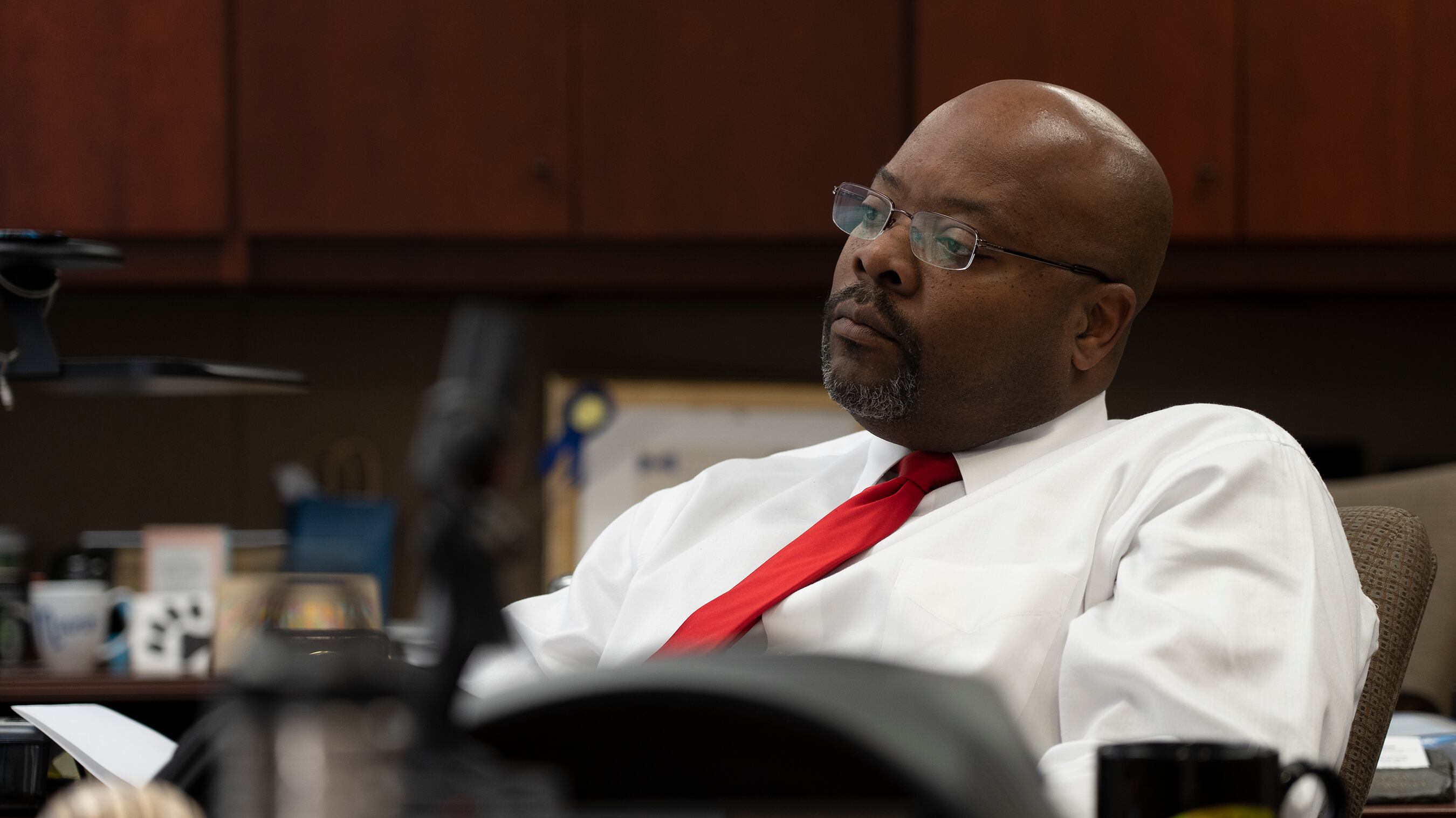 Aurora Superintendent Rico Munn, wearing a white dress shirt and red tie, leans back in his chair and appears to be listening intently to someone or something. His face is serious.