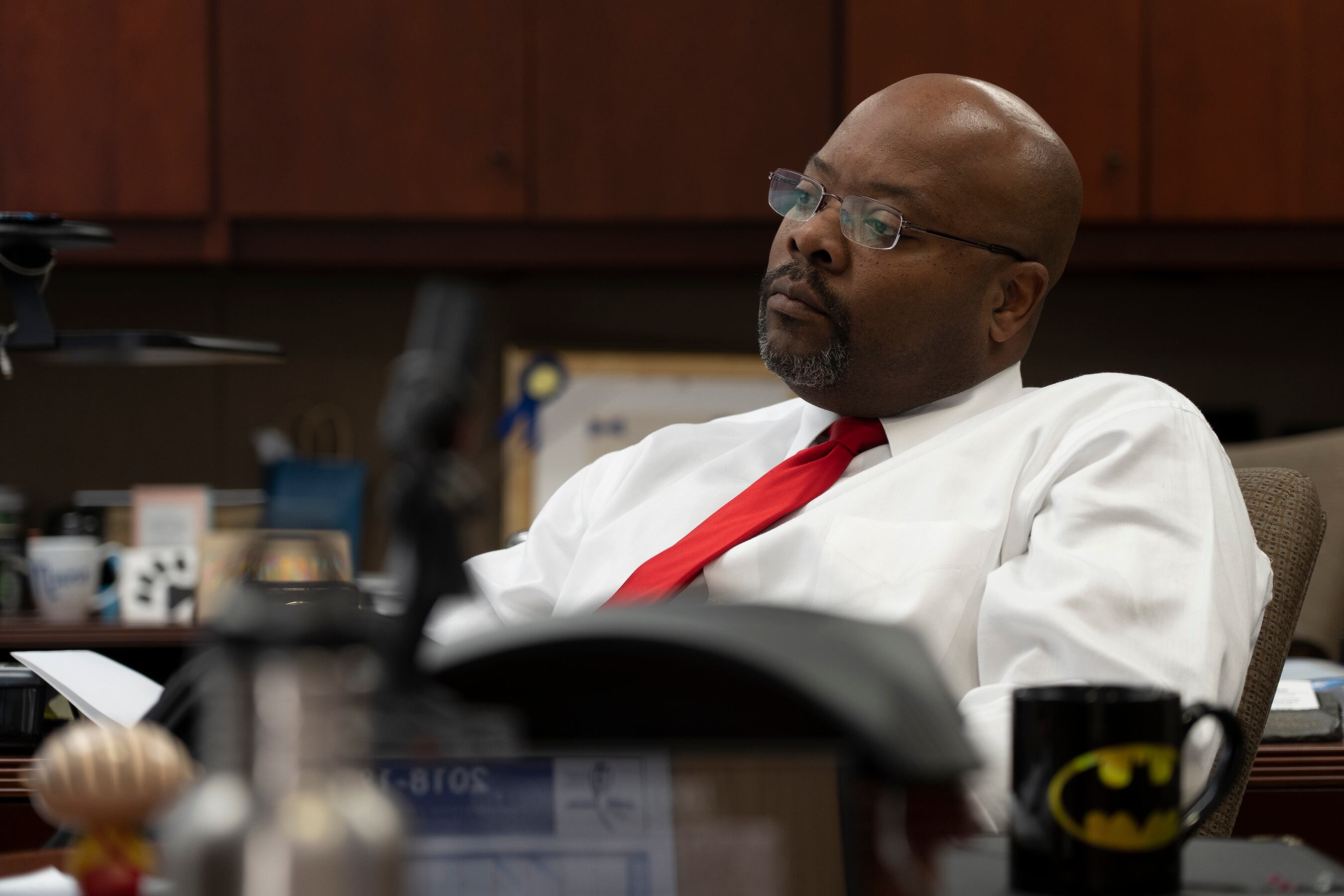 Aurora Superintendent Rico Munn, wearing a white dress shirt and red tie, leans back in his chair and appears to be listening intently to someone or something. His face is serious.
