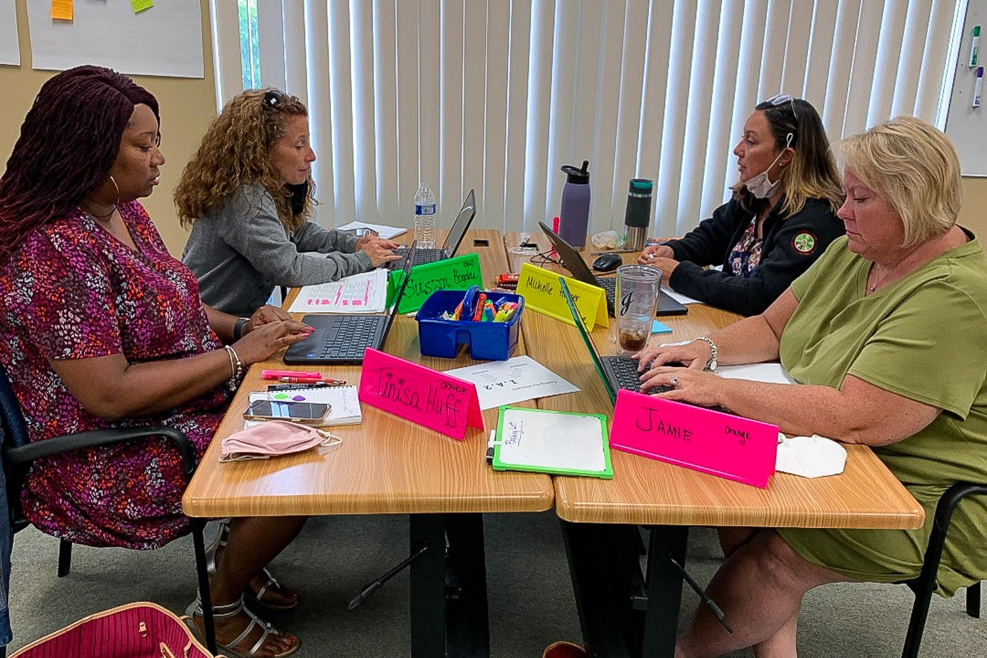 Four teachers from Forest Park sit at tables and work on laptops during professional development training.