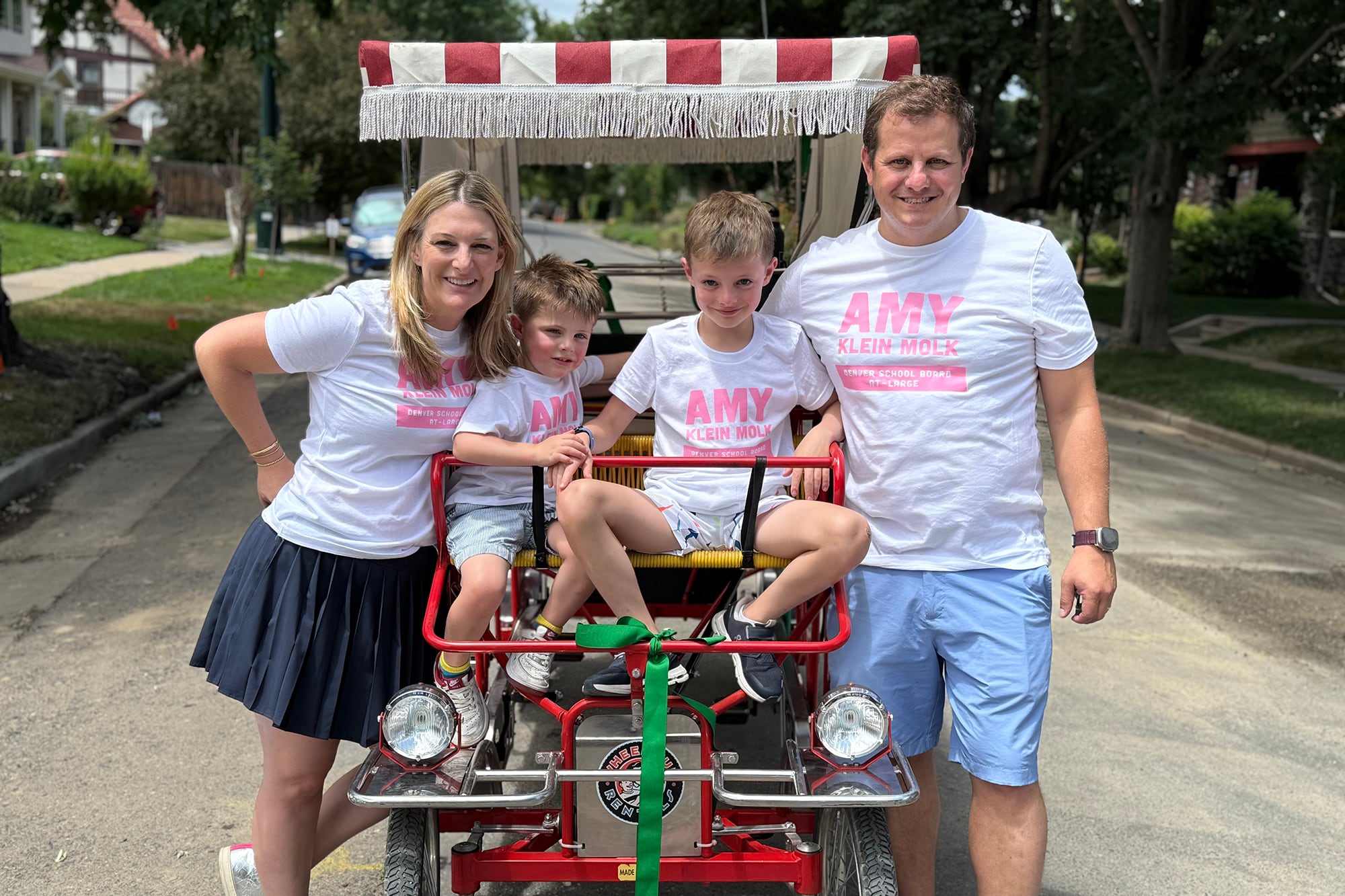 A photograph of a white family with the mom on the left, two young sons in the middle and the dad on the far right outside.