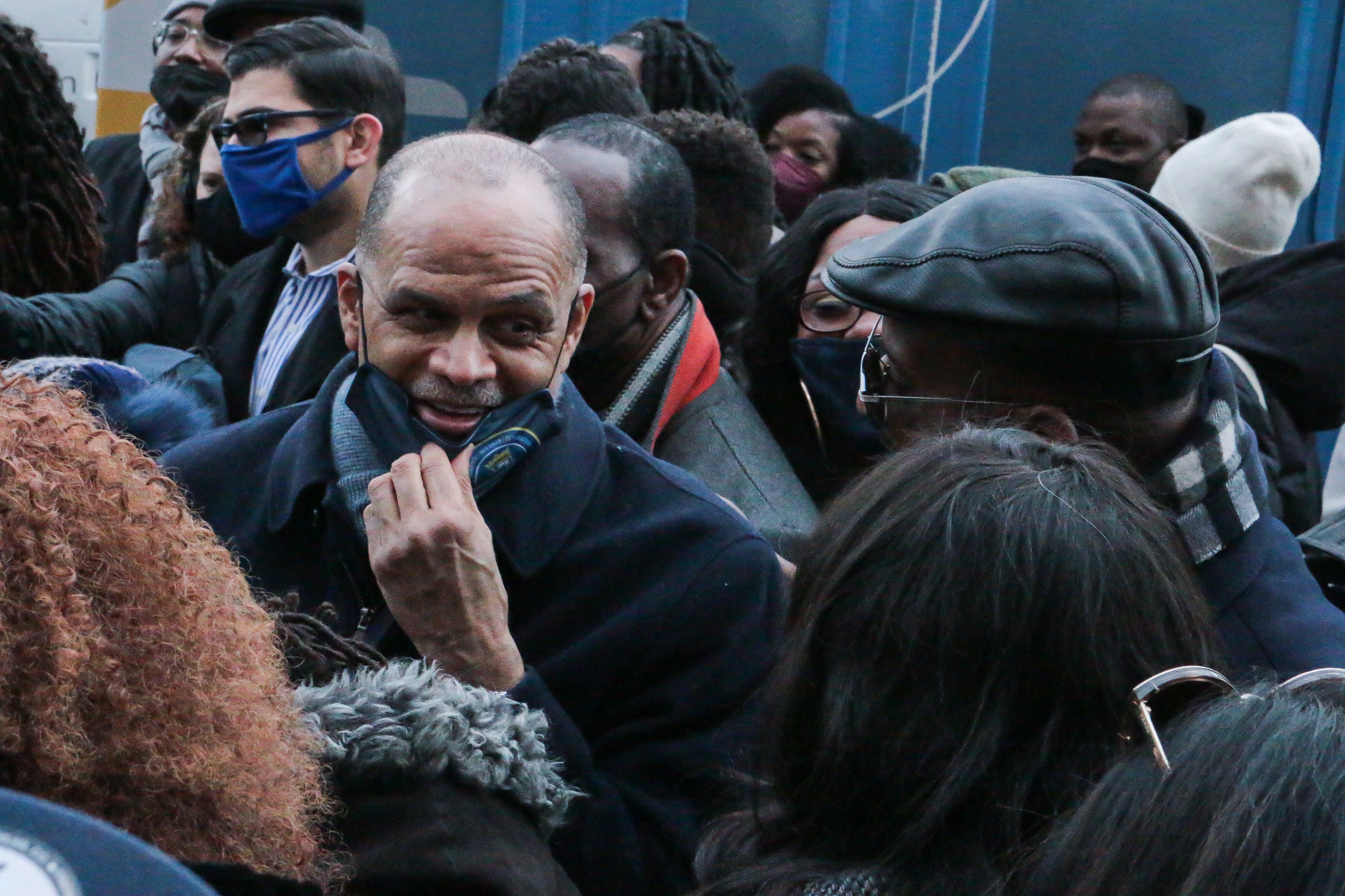 A man in a black coat surrounded by other people, most of them without their faces visible.
