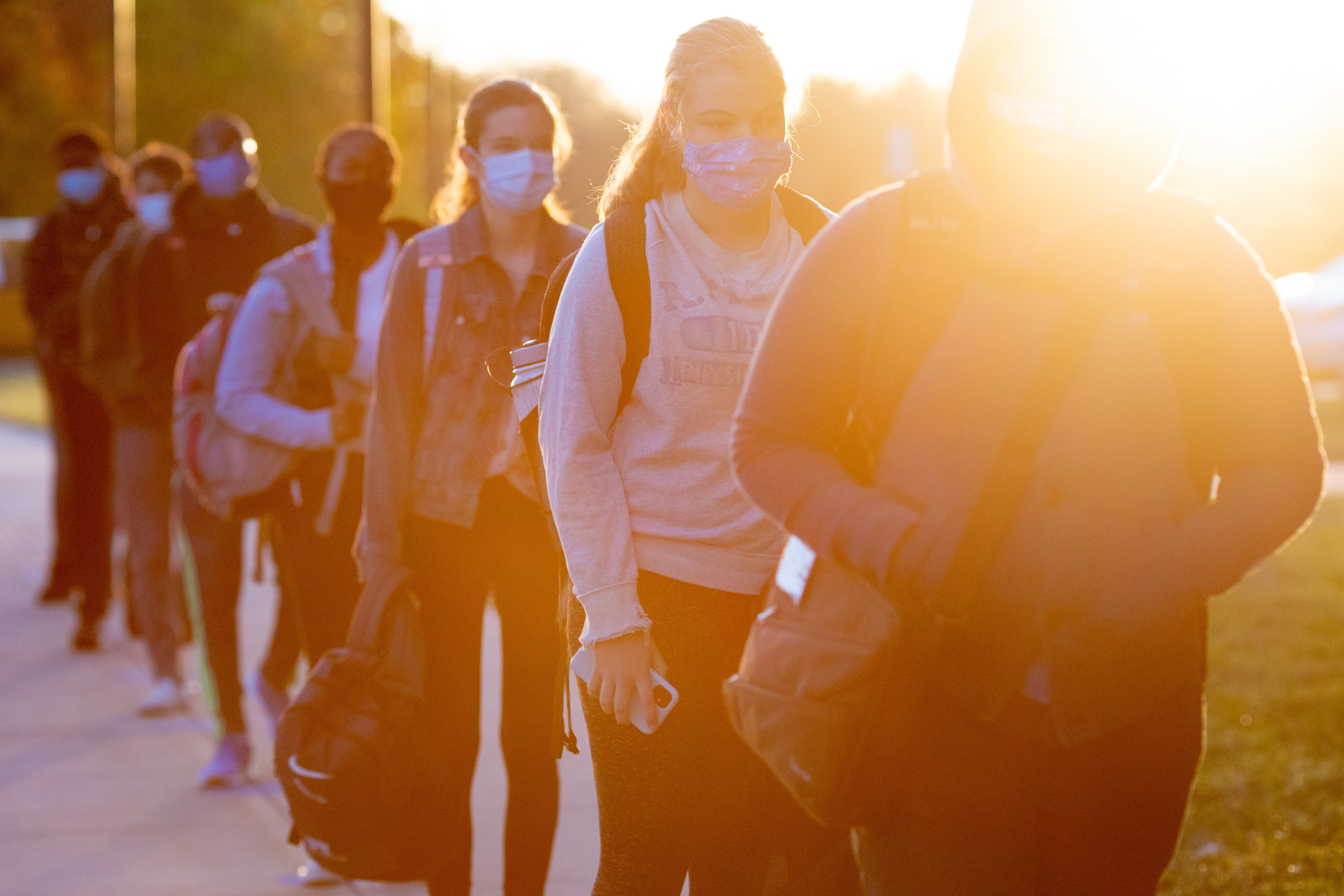 Students line up on socially distanced dots painted on the sidewalk to wait their turn to be scanned by a temperature screener before classes.
