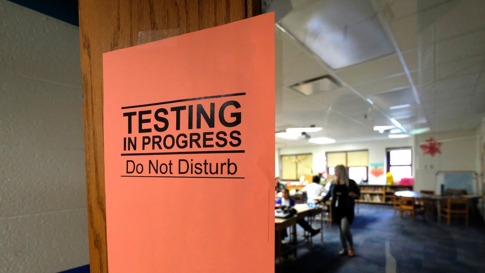 An orange sign says “testing in progress, do not disturb” as students work in the background.