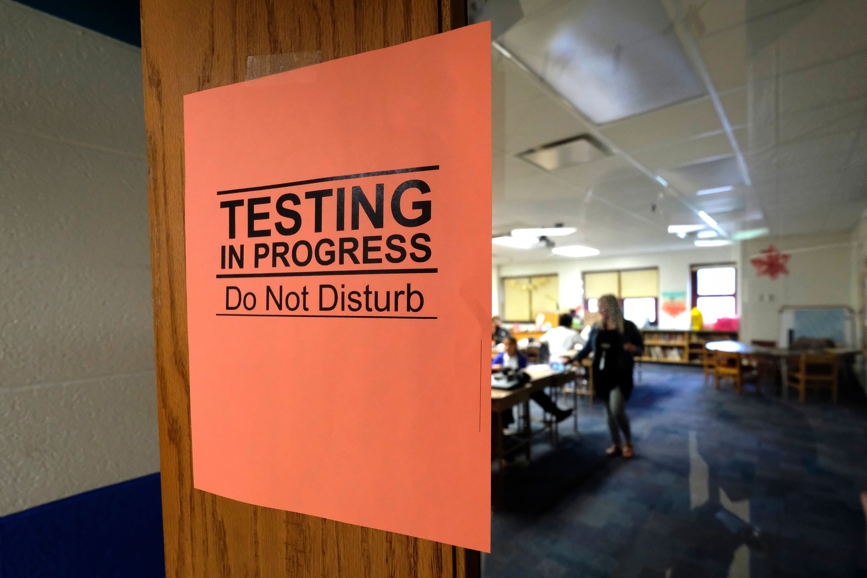 An orange sign says “testing in progress, do not disturb” as students work in the background.