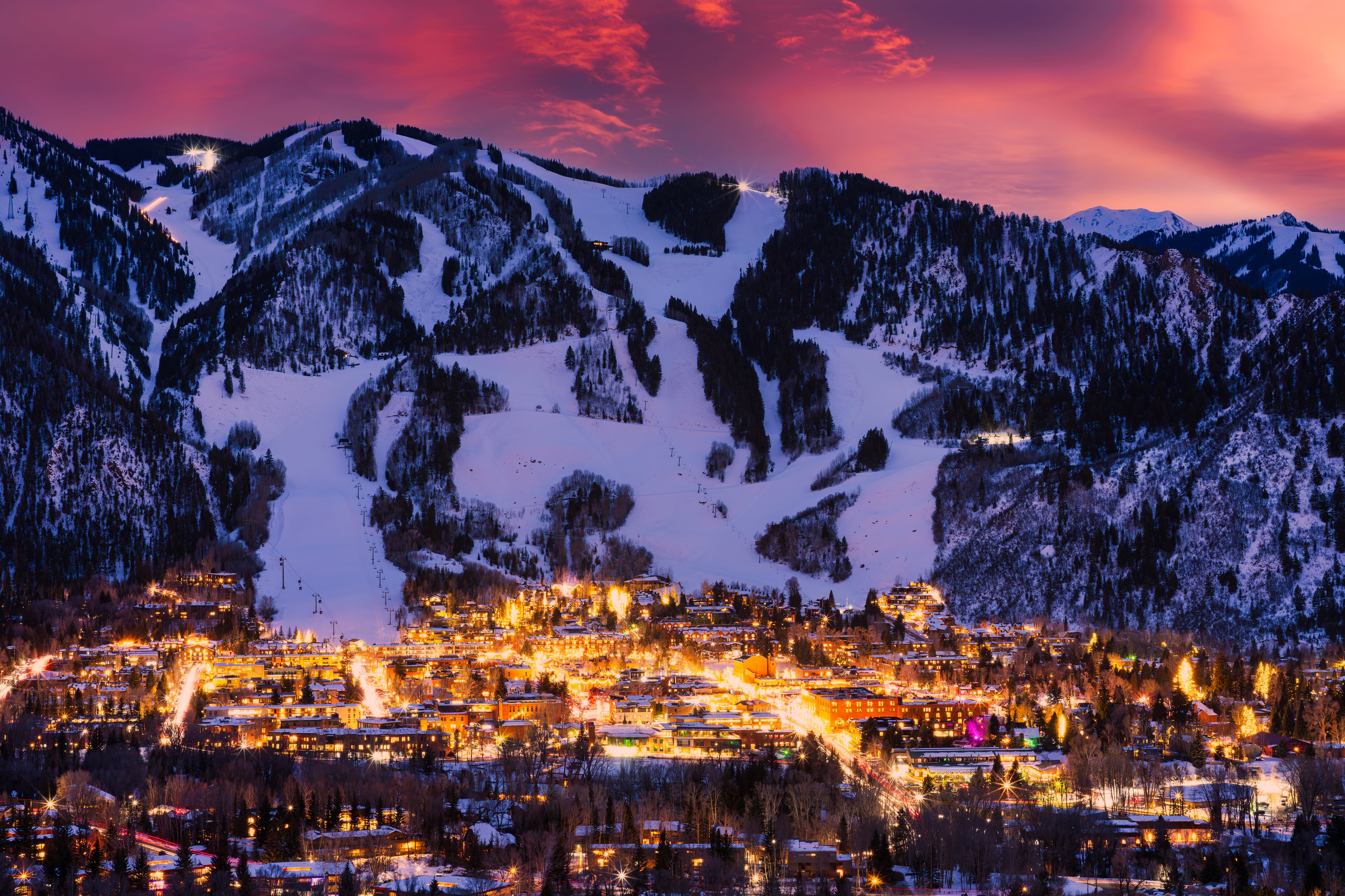 A downtown is lit up in front of a snow-covered mountain.