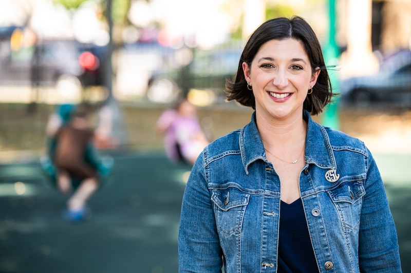 A woman in a jeans jacket stands.