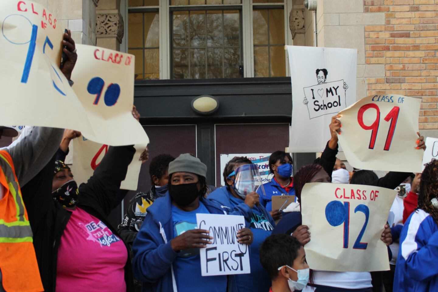 People hold up signs saying “Class of 90,” “Class of 91” and “Class at 92” at rally