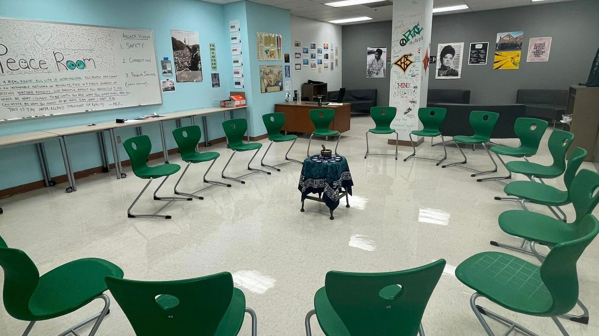 Several green chairs are arranged in an oval in a room with gray walls and a whiteboard.