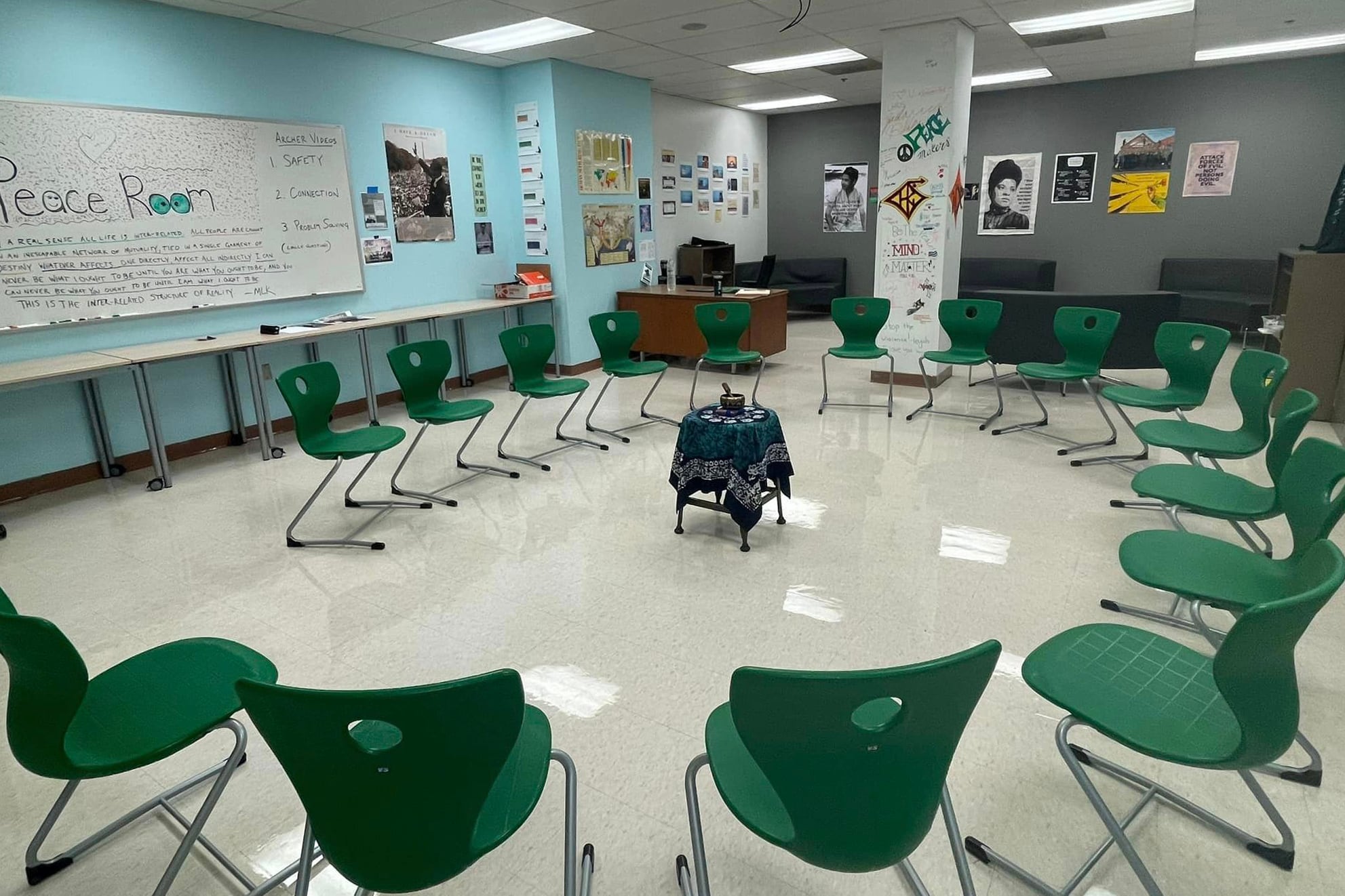 Several green chairs are arranged in an oval in a room with gray walls and a whiteboard.
